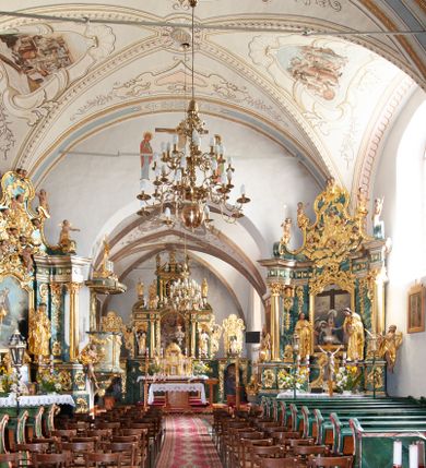 Zdjęcie nr 11: Kościół orientowany, murowany z kamienia, jednonawowy, z prostokątną, trójprzęsłową nawą oraz węższym dwuprzęsłowym prezbiterium zamkniętym prosto, z prostokątną zakrystią przy północnej ścianie. Od zachodu wieża na planie kwadratu, do północnej ściany nawy dobudowana kaplica na rzucie kwadratu o ściętych narożach, do południowej niewielka kruchta na planie kwadratu. Prezbiterium nakryte sklepieniem krzyżowo-żebrowym z dwoma zwornikami. 
Nawa sklepiona krzyżowo, przęsła wydzielone arkadami wspartymi na półfilarach. Otwór tęczowy w formie stojącego prostokąta zamkniętego łukiem półkolistym. W zachodniej części nawy parapet chóru muzycznego, z wybrzuszoną środkową częścią balustrady, wsparty na czterech kolumnach. 
Fasada wieżowa, z wejściem na osi. Wieża smukła, bez podziałów architektonicznych, zakończona profilowanym gzymsem, wyłamującym się na każdej ścianie na kształt łuku odcinkowego. W najwyższej partii ścian, z trzech stron, okna w formie stojącego prostokąta zamkniętego półkoliście. Wieża zwieńczona hełmem baniastym z latarnią, pokrytym gontem. 
Kościół opięty szkarpami dwuuskokowymi, nakrytymi daszkami gontowymi. W elewacji południowej pomiędzy szkarpami pięć wąskich okien w formie stojącego prostokąta zamkniętego łukiem półkolistym. Na wschodniej dobudowany ogrojec w formie masywnej arkady, zamkniętej dwuspadowym daszkiem z ołtarzem i krucyfiksem. Nawa i prezbiterium nakryte osobnymi dachami dwuspadowymi, gontowymi. Nad prezbiterium drewniana wieżyczka na sygnaturkę, z latarnią, zwieńczona hełmem baniastym. Kaplica przykryta dachem gontowych, trójspadowym, kruchta zaś pulpitowym. 
Kościół otoczony niskim murem kamiennym, nakrytym daszkiem gontowym. Od wschodu dwie bramy flankowane filarami z wazonami. 

