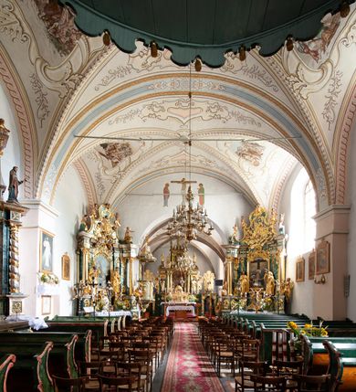 Zdjęcie nr 8: Kościół orientowany, murowany z kamienia, jednonawowy, z prostokątną, trójprzęsłową nawą oraz węższym dwuprzęsłowym prezbiterium zamkniętym prosto, z prostokątną zakrystią przy północnej ścianie. Od zachodu wieża na planie kwadratu, do północnej ściany nawy dobudowana kaplica na rzucie kwadratu o ściętych narożach, do południowej niewielka kruchta na planie kwadratu. Prezbiterium nakryte sklepieniem krzyżowo-żebrowym z dwoma zwornikami. 
Nawa sklepiona krzyżowo, przęsła wydzielone arkadami wspartymi na półfilarach. Otwór tęczowy w formie stojącego prostokąta zamkniętego łukiem półkolistym. W zachodniej części nawy parapet chóru muzycznego, z wybrzuszoną środkową częścią balustrady, wsparty na czterech kolumnach. 
Fasada wieżowa, z wejściem na osi. Wieża smukła, bez podziałów architektonicznych, zakończona profilowanym gzymsem, wyłamującym się na każdej ścianie na kształt łuku odcinkowego. W najwyższej partii ścian, z trzech stron, okna w formie stojącego prostokąta zamkniętego półkoliście. Wieża zwieńczona hełmem baniastym z latarnią, pokrytym gontem. 
Kościół opięty szkarpami dwuuskokowymi, nakrytymi daszkami gontowymi. W elewacji południowej pomiędzy szkarpami pięć wąskich okien w formie stojącego prostokąta zamkniętego łukiem półkolistym. Na wschodniej dobudowany ogrojec w formie masywnej arkady, zamkniętej dwuspadowym daszkiem z ołtarzem i krucyfiksem. Nawa i prezbiterium nakryte osobnymi dachami dwuspadowymi, gontowymi. Nad prezbiterium drewniana wieżyczka na sygnaturkę, z latarnią, zwieńczona hełmem baniastym. Kaplica przykryta dachem gontowych, trójspadowym, kruchta zaś pulpitowym. 
Kościół otoczony niskim murem kamiennym, nakrytym daszkiem gontowym. Od wschodu dwie bramy flankowane filarami z wazonami. 

