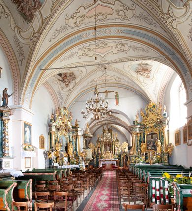 Zdjęcie nr 6: Kościół orientowany, murowany z kamienia, jednonawowy, z prostokątną, trójprzęsłową nawą oraz węższym dwuprzęsłowym prezbiterium zamkniętym prosto, z prostokątną zakrystią przy północnej ścianie. Od zachodu wieża na planie kwadratu, do północnej ściany nawy dobudowana kaplica na rzucie kwadratu o ściętych narożach, do południowej niewielka kruchta na planie kwadratu. Prezbiterium nakryte sklepieniem krzyżowo-żebrowym z dwoma zwornikami. 
Nawa sklepiona krzyżowo, przęsła wydzielone arkadami wspartymi na półfilarach. Otwór tęczowy w formie stojącego prostokąta zamkniętego łukiem półkolistym. W zachodniej części nawy parapet chóru muzycznego, z wybrzuszoną środkową częścią balustrady, wsparty na czterech kolumnach. 
Fasada wieżowa, z wejściem na osi. Wieża smukła, bez podziałów architektonicznych, zakończona profilowanym gzymsem, wyłamującym się na każdej ścianie na kształt łuku odcinkowego. W najwyższej partii ścian, z trzech stron, okna w formie stojącego prostokąta zamkniętego półkoliście. Wieża zwieńczona hełmem baniastym z latarnią, pokrytym gontem. 
Kościół opięty szkarpami dwuuskokowymi, nakrytymi daszkami gontowymi. W elewacji południowej pomiędzy szkarpami pięć wąskich okien w formie stojącego prostokąta zamkniętego łukiem półkolistym. Na wschodniej dobudowany ogrojec w formie masywnej arkady, zamkniętej dwuspadowym daszkiem z ołtarzem i krucyfiksem. Nawa i prezbiterium nakryte osobnymi dachami dwuspadowymi, gontowymi. Nad prezbiterium drewniana wieżyczka na sygnaturkę, z latarnią, zwieńczona hełmem baniastym. Kaplica przykryta dachem gontowych, trójspadowym, kruchta zaś pulpitowym. 
Kościół otoczony niskim murem kamiennym, nakrytym daszkiem gontowym. Od wschodu dwie bramy flankowane filarami z wazonami. 

