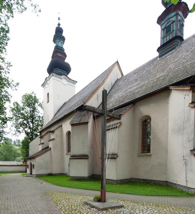 Zdjęcie nr 13: Kościół orientowany, murowany z kamienia, jednonawowy, z prostokątną, trójprzęsłową nawą oraz węższym dwuprzęsłowym prezbiterium zamkniętym prosto, z prostokątną zakrystią przy północnej ścianie. Od zachodu wieża na planie kwadratu, do północnej ściany nawy dobudowana kaplica na rzucie kwadratu o ściętych narożach, do południowej niewielka kruchta na planie kwadratu. Prezbiterium nakryte sklepieniem krzyżowo-żebrowym z dwoma zwornikami. 
Nawa sklepiona krzyżowo, przęsła wydzielone arkadami wspartymi na półfilarach. Otwór tęczowy w formie stojącego prostokąta zamkniętego łukiem półkolistym. W zachodniej części nawy parapet chóru muzycznego, z wybrzuszoną środkową częścią balustrady, wsparty na czterech kolumnach. 
Fasada wieżowa, z wejściem na osi. Wieża smukła, bez podziałów architektonicznych, zakończona profilowanym gzymsem, wyłamującym się na każdej ścianie na kształt łuku odcinkowego. W najwyższej partii ścian, z trzech stron, okna w formie stojącego prostokąta zamkniętego półkoliście. Wieża zwieńczona hełmem baniastym z latarnią, pokrytym gontem. 
Kościół opięty szkarpami dwuuskokowymi, nakrytymi daszkami gontowymi. W elewacji południowej pomiędzy szkarpami pięć wąskich okien w formie stojącego prostokąta zamkniętego łukiem półkolistym. Na wschodniej dobudowany ogrojec w formie masywnej arkady, zamkniętej dwuspadowym daszkiem z ołtarzem i krucyfiksem. Nawa i prezbiterium nakryte osobnymi dachami dwuspadowymi, gontowymi. Nad prezbiterium drewniana wieżyczka na sygnaturkę, z latarnią, zwieńczona hełmem baniastym. Kaplica przykryta dachem gontowych, trójspadowym, kruchta zaś pulpitowym. 
Kościół otoczony niskim murem kamiennym, nakrytym daszkiem gontowym. Od wschodu dwie bramy flankowane filarami z wazonami. 

