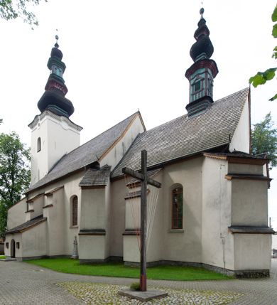 Zdjęcie nr 1: Kościół orientowany, murowany z kamienia, jednonawowy, z prostokątną, trójprzęsłową nawą oraz węższym dwuprzęsłowym prezbiterium zamkniętym prosto, z prostokątną zakrystią przy północnej ścianie. Od zachodu wieża na planie kwadratu, do północnej ściany nawy dobudowana kaplica na rzucie kwadratu o ściętych narożach, do południowej niewielka kruchta na planie kwadratu. Prezbiterium nakryte sklepieniem krzyżowo-żebrowym z dwoma zwornikami. 
Nawa sklepiona krzyżowo, przęsła wydzielone arkadami wspartymi na półfilarach. Otwór tęczowy w formie stojącego prostokąta zamkniętego łukiem półkolistym. W zachodniej części nawy parapet chóru muzycznego, z wybrzuszoną środkową częścią balustrady, wsparty na czterech kolumnach. 
Fasada wieżowa, z wejściem na osi. Wieża smukła, bez podziałów architektonicznych, zakończona profilowanym gzymsem, wyłamującym się na każdej ścianie na kształt łuku odcinkowego. W najwyższej partii ścian, z trzech stron, okna w formie stojącego prostokąta zamkniętego półkoliście. Wieża zwieńczona hełmem baniastym z latarnią, pokrytym gontem. 
Kościół opięty szkarpami dwuuskokowymi, nakrytymi daszkami gontowymi. W elewacji południowej pomiędzy szkarpami pięć wąskich okien w formie stojącego prostokąta zamkniętego łukiem półkolistym. Na wschodniej dobudowany ogrojec w formie masywnej arkady, zamkniętej dwuspadowym daszkiem z ołtarzem i krucyfiksem. Nawa i prezbiterium nakryte osobnymi dachami dwuspadowymi, gontowymi. Nad prezbiterium drewniana wieżyczka na sygnaturkę, z latarnią, zwieńczona hełmem baniastym. Kaplica przykryta dachem gontowych, trójspadowym, kruchta zaś pulpitowym. 
Kościół otoczony niskim murem kamiennym, nakrytym daszkiem gontowym. Od wschodu dwie bramy flankowane filarami z wazonami. 

