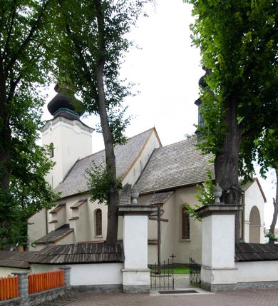 Zdjęcie nr 30: Kościół orientowany, murowany z kamienia, jednonawowy, z prostokątną, trójprzęsłową nawą oraz węższym dwuprzęsłowym prezbiterium zamkniętym prosto, z prostokątną zakrystią przy północnej ścianie. Od zachodu wieża na planie kwadratu, do północnej ściany nawy dobudowana kaplica na rzucie kwadratu o ściętych narożach, do południowej niewielka kruchta na planie kwadratu. Prezbiterium nakryte sklepieniem krzyżowo-żebrowym z dwoma zwornikami. 
Nawa sklepiona krzyżowo, przęsła wydzielone arkadami wspartymi na półfilarach. Otwór tęczowy w formie stojącego prostokąta zamkniętego łukiem półkolistym. W zachodniej części nawy parapet chóru muzycznego, z wybrzuszoną środkową częścią balustrady, wsparty na czterech kolumnach. 
Fasada wieżowa, z wejściem na osi. Wieża smukła, bez podziałów architektonicznych, zakończona profilowanym gzymsem, wyłamującym się na każdej ścianie na kształt łuku odcinkowego. W najwyższej partii ścian, z trzech stron, okna w formie stojącego prostokąta zamkniętego półkoliście. Wieża zwieńczona hełmem baniastym z latarnią, pokrytym gontem. 
Kościół opięty szkarpami dwuuskokowymi, nakrytymi daszkami gontowymi. W elewacji południowej pomiędzy szkarpami pięć wąskich okien w formie stojącego prostokąta zamkniętego łukiem półkolistym. Na wschodniej dobudowany ogrojec w formie masywnej arkady, zamkniętej dwuspadowym daszkiem z ołtarzem i krucyfiksem. Nawa i prezbiterium nakryte osobnymi dachami dwuspadowymi, gontowymi. Nad prezbiterium drewniana wieżyczka na sygnaturkę, z latarnią, zwieńczona hełmem baniastym. Kaplica przykryta dachem gontowych, trójspadowym, kruchta zaś pulpitowym. 
Kościół otoczony niskim murem kamiennym, nakrytym daszkiem gontowym. Od wschodu dwie bramy flankowane filarami z wazonami. 

