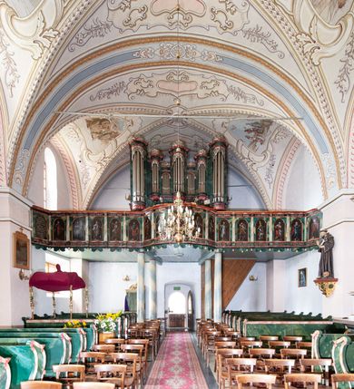 Zdjęcie nr 14: Kościół orientowany, murowany z kamienia, jednonawowy, z prostokątną, trójprzęsłową nawą oraz węższym dwuprzęsłowym prezbiterium zamkniętym prosto, z prostokątną zakrystią przy północnej ścianie. Od zachodu wieża na planie kwadratu, do północnej ściany nawy dobudowana kaplica na rzucie kwadratu o ściętych narożach, do południowej niewielka kruchta na planie kwadratu. Prezbiterium nakryte sklepieniem krzyżowo-żebrowym z dwoma zwornikami. 
Nawa sklepiona krzyżowo, przęsła wydzielone arkadami wspartymi na półfilarach. Otwór tęczowy w formie stojącego prostokąta zamkniętego łukiem półkolistym. W zachodniej części nawy parapet chóru muzycznego, z wybrzuszoną środkową częścią balustrady, wsparty na czterech kolumnach. 
Fasada wieżowa, z wejściem na osi. Wieża smukła, bez podziałów architektonicznych, zakończona profilowanym gzymsem, wyłamującym się na każdej ścianie na kształt łuku odcinkowego. W najwyższej partii ścian, z trzech stron, okna w formie stojącego prostokąta zamkniętego półkoliście. Wieża zwieńczona hełmem baniastym z latarnią, pokrytym gontem. 
Kościół opięty szkarpami dwuuskokowymi, nakrytymi daszkami gontowymi. W elewacji południowej pomiędzy szkarpami pięć wąskich okien w formie stojącego prostokąta zamkniętego łukiem półkolistym. Na wschodniej dobudowany ogrojec w formie masywnej arkady, zamkniętej dwuspadowym daszkiem z ołtarzem i krucyfiksem. Nawa i prezbiterium nakryte osobnymi dachami dwuspadowymi, gontowymi. Nad prezbiterium drewniana wieżyczka na sygnaturkę, z latarnią, zwieńczona hełmem baniastym. Kaplica przykryta dachem gontowych, trójspadowym, kruchta zaś pulpitowym. 
Kościół otoczony niskim murem kamiennym, nakrytym daszkiem gontowym. Od wschodu dwie bramy flankowane filarami z wazonami. 

