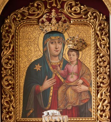 Zdjęcie nr 1: Para koron (większa – Marii, mniejsza – Dzieciątka), nałożonych na obraz Matki Boskiej z Dzieciątkiem. Obie korony zakomponowane i ozdobione analogicznie: u dołu wygięte lekko ku górze otoki, uformowane z szerokiej taśmy, dekorowanej kaboszonami, rautami i nałożonymi osobno kamieniami w oprawach (pojedynczo i na koronie Matki Boskiej parami). Z otoków wyrastają po dwie pary większych i mniejszych kabłąków, mocno wygiętych, tworzących ażurowe układy wzbogacone na osi każdej korony krótkim, rozszerzającym się ku dołowi kabłąkiem. U podstawy każdego kabłąku pęki mięsistych liści, powierzchnia kabłąków ozdobiona jak otok (kamienie występują tylko pojedynczo), ze szrafowaniem w tle. Obie korony wieńczą kule z krzyżami równoramiennymi na szczycie. Kamienie zdobiące korony są półprzezroczyste, w kolorach niebieskim i czerwonym.