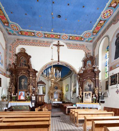 Zdjęcie nr 10: Kościół orientowany, jednonawowy, z krótkim zakończonym wielobocznie prezbiterium, przy którym od północy zakrystia z nowszym przedsionkiem; przy nawie od północy prostokątna kaplica Różańcowa (1712 r.), od zachodu wieża na rzucie kwadratu, od południa drewniana kruchta. Wewnątrz stropy. Arkada tęczy szeroka półkolista. Zewnątrz mury opięte przyporami, tynkowane. Dachy dwuspadowe i pulpitowe. Na kalenicy dachu nawy wieżyczka na sygnaturkę z datą 1878. Okna prostokątne zamknięte półkoliście. Dwa portale kamienne prostokątne. Wieża dołem gotycka, nadbudowana w stylu pseudoromańskim; trójkondygnacyjna, dołem z narożnikami artykułowanymi boniowaniem, narożniki górnej kondygnacji ujęte lizenami połączonymi fryzem arkadkowym. Elewacje wieży zwieńczone trójkątnymi szczytami i ostrosłupowym hełmem krytym blachą.