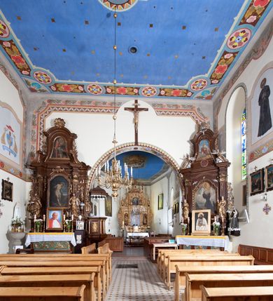 Zdjęcie nr 9: Kościół orientowany, jednonawowy, z krótkim zakończonym wielobocznie prezbiterium, przy którym od północy zakrystia z nowszym przedsionkiem; przy nawie od północy prostokątna kaplica Różańcowa (1712 r.), od zachodu wieża na rzucie kwadratu, od południa drewniana kruchta. Wewnątrz stropy. Arkada tęczy szeroka półkolista. Zewnątrz mury opięte przyporami, tynkowane. Dachy dwuspadowe i pulpitowe. Na kalenicy dachu nawy wieżyczka na sygnaturkę z datą 1878. Okna prostokątne zamknięte półkoliście. Dwa portale kamienne prostokątne. Wieża dołem gotycka, nadbudowana w stylu pseudoromańskim; trójkondygnacyjna, dołem z narożnikami artykułowanymi boniowaniem, narożniki górnej kondygnacji ujęte lizenami połączonymi fryzem arkadkowym. Elewacje wieży zwieńczone trójkątnymi szczytami i ostrosłupowym hełmem krytym blachą.