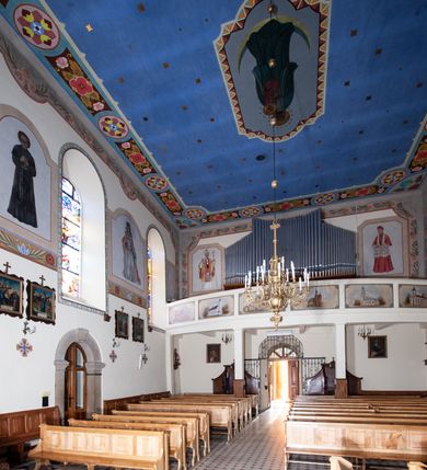 Zdjęcie nr 14: Kościół orientowany, jednonawowy, z krótkim zakończonym wielobocznie prezbiterium, przy którym od północy zakrystia z nowszym przedsionkiem; przy nawie od północy prostokątna kaplica Różańcowa (1712 r.), od zachodu wieża na rzucie kwadratu, od południa drewniana kruchta. Wewnątrz stropy. Arkada tęczy szeroka półkolista. Zewnątrz mury opięte przyporami, tynkowane. Dachy dwuspadowe i pulpitowe. Na kalenicy dachu nawy wieżyczka na sygnaturkę z datą 1878. Okna prostokątne zamknięte półkoliście. Dwa portale kamienne prostokątne. Wieża dołem gotycka, nadbudowana w stylu pseudoromańskim; trójkondygnacyjna, dołem z narożnikami artykułowanymi boniowaniem, narożniki górnej kondygnacji ujęte lizenami połączonymi fryzem arkadkowym. Elewacje wieży zwieńczone trójkątnymi szczytami i ostrosłupowym hełmem krytym blachą.