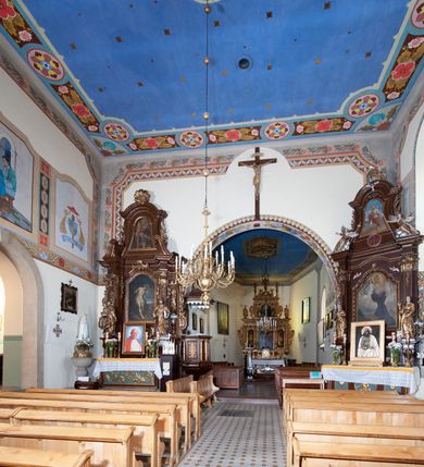 Zdjęcie nr 8: Kościół orientowany, jednonawowy, z krótkim zakończonym wielobocznie prezbiterium, przy którym od północy zakrystia z nowszym przedsionkiem; przy nawie od północy prostokątna kaplica Różańcowa (1712 r.), od zachodu wieża na rzucie kwadratu, od południa drewniana kruchta. Wewnątrz stropy. Arkada tęczy szeroka półkolista. Zewnątrz mury opięte przyporami, tynkowane. Dachy dwuspadowe i pulpitowe. Na kalenicy dachu nawy wieżyczka na sygnaturkę z datą 1878. Okna prostokątne zamknięte półkoliście. Dwa portale kamienne prostokątne. Wieża dołem gotycka, nadbudowana w stylu pseudoromańskim; trójkondygnacyjna, dołem z narożnikami artykułowanymi boniowaniem, narożniki górnej kondygnacji ujęte lizenami połączonymi fryzem arkadkowym. Elewacje wieży zwieńczone trójkątnymi szczytami i ostrosłupowym hełmem krytym blachą.