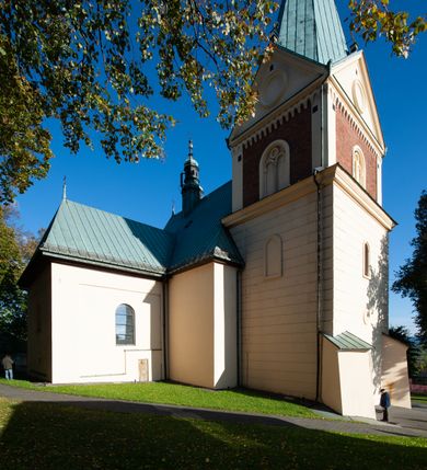 Zdjęcie nr 21: Kościół orientowany, jednonawowy, z krótkim zakończonym wielobocznie prezbiterium, przy którym od północy zakrystia z nowszym przedsionkiem; przy nawie od północy prostokątna kaplica Różańcowa (1712 r.), od zachodu wieża na rzucie kwadratu, od południa drewniana kruchta. Wewnątrz stropy. Arkada tęczy szeroka półkolista. Zewnątrz mury opięte przyporami, tynkowane. Dachy dwuspadowe i pulpitowe. Na kalenicy dachu nawy wieżyczka na sygnaturkę z datą 1878. Okna prostokątne zamknięte półkoliście. Dwa portale kamienne prostokątne. Wieża dołem gotycka, nadbudowana w stylu pseudoromańskim; trójkondygnacyjna, dołem z narożnikami artykułowanymi boniowaniem, narożniki górnej kondygnacji ujęte lizenami połączonymi fryzem arkadkowym. Elewacje wieży zwieńczone trójkątnymi szczytami i ostrosłupowym hełmem krytym blachą.