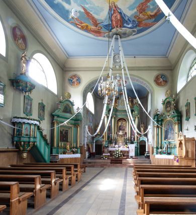 Zdjęcie nr 20: Kościół murowany, składa się z nawy i zwróconego na południe prezbiterium, do którego przylega zakrystia, nad którą znajduje się skarbiec; od północy wieża. Prezbiterium jest węższe od nawy, o zaokrąglonych narożach, oddzielone od prostokątnej nawy łukiem tęczowym. Ściany kościoła gładkie, przeprute półkolistymi oknami – dwoma w prezbiterium, sześcioma w nawie. Od zachodu chór wsparty na dwóch kolumnach, z balustradą wyłamaną na środku, dekorowaną u spodu lambrekinem. Ściany kościoła gładkie, w dolnej partii osłonięte drewnianą boazerią, z wnęką na chrzcielnicę po lewej i drugą na drzwi z prawej strony. Wnętrze przekrywają stropy – zwierciadlany w prezbiterium i płaski  z fasetami w nawie. Na nich oraz w górnej partii ścian polichromia. Nad prezbiterium wizerunek zmartwychwstałego Chrystusa, nad nawą zakomponowana w kole scena adoracji Najświętszej Marii Panny przez apostołów, poniżej, na ścianach medaliony z postaciami ważnych osobistości, świętych i aniołów. Główne drzwi od północy, boczne od zachodu. 
Kościół posadowiony na cokole. Elewacja frontowa ze zdwojonym ryzalitem, którego środek odpowiada szerokości wieży; podziały poziome przeprowadzone przy pomocy gzymsów. Na osi wejście i  okno, oba w boniowanym obramieniu. Okno ujmuje polichromowana scena Zwiastowania. Ryzalit wieńczy trójkątny fronton. Cofnięty ryzalit w dolnej partii boniowany, wyżej gładki, zwieńczony ćwierćkolistymi fragmentami przerwanego przyczółka. Boki elewacji frontowej gładkie, zwieńczone frontonem przerwanym na masyw czworobocznej wieży przeprutej z każdej strony oknem w kształcie stojącego prostokąta zamkniętego łukiem pełnym. Elewacje boczne gładkie, przeprute półkolistymi oknami. Od wschodu poniżej okien szare płyciny, od południa, w kapliczkowej oprawie grupa Ukrzyżowania. Dach nad nawą dwuspadowy, nad prezbiterium trójspadowy, dach wieńczy baniasty hełm z latarnią zakończony krzyżem, na kalenicy barokowa wieżyczka na sygnaturkę. 
