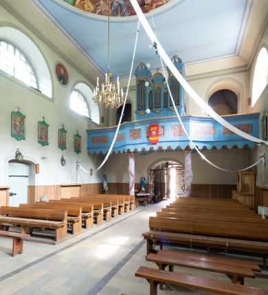 Zdjęcie nr 27: Kościół murowany, składa się z nawy i zwróconego na południe prezbiterium, do którego przylega zakrystia, nad którą znajduje się skarbiec; od północy wieża. Prezbiterium jest węższe od nawy, o zaokrąglonych narożach, oddzielone od prostokątnej nawy łukiem tęczowym. Ściany kościoła gładkie, przeprute półkolistymi oknami – dwoma w prezbiterium, sześcioma w nawie. Od zachodu chór wsparty na dwóch kolumnach, z balustradą wyłamaną na środku, dekorowaną u spodu lambrekinem. Ściany kościoła gładkie, w dolnej partii osłonięte drewnianą boazerią, z wnęką na chrzcielnicę po lewej i drugą na drzwi z prawej strony. Wnętrze przekrywają stropy – zwierciadlany w prezbiterium i płaski  z fasetami w nawie. Na nich oraz w górnej partii ścian polichromia. Nad prezbiterium wizerunek zmartwychwstałego Chrystusa, nad nawą zakomponowana w kole scena adoracji Najświętszej Marii Panny przez apostołów, poniżej, na ścianach medaliony z postaciami ważnych osobistości, świętych i aniołów. Główne drzwi od północy, boczne od zachodu. 
Kościół posadowiony na cokole. Elewacja frontowa ze zdwojonym ryzalitem, którego środek odpowiada szerokości wieży; podziały poziome przeprowadzone przy pomocy gzymsów. Na osi wejście i  okno, oba w boniowanym obramieniu. Okno ujmuje polichromowana scena Zwiastowania. Ryzalit wieńczy trójkątny fronton. Cofnięty ryzalit w dolnej partii boniowany, wyżej gładki, zwieńczony ćwierćkolistymi fragmentami przerwanego przyczółka. Boki elewacji frontowej gładkie, zwieńczone frontonem przerwanym na masyw czworobocznej wieży przeprutej z każdej strony oknem w kształcie stojącego prostokąta zamkniętego łukiem pełnym. Elewacje boczne gładkie, przeprute półkolistymi oknami. Od wschodu poniżej okien szare płyciny, od południa, w kapliczkowej oprawie grupa Ukrzyżowania. Dach nad nawą dwuspadowy, nad prezbiterium trójspadowy, dach wieńczy baniasty hełm z latarnią zakończony krzyżem, na kalenicy barokowa wieżyczka na sygnaturkę. 

