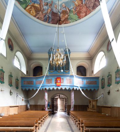 Zdjęcie nr 23: Kościół murowany, składa się z nawy i zwróconego na południe prezbiterium, do którego przylega zakrystia, nad którą znajduje się skarbiec; od północy wieża. Prezbiterium jest węższe od nawy, o zaokrąglonych narożach, oddzielone od prostokątnej nawy łukiem tęczowym. Ściany kościoła gładkie, przeprute półkolistymi oknami – dwoma w prezbiterium, sześcioma w nawie. Od zachodu chór wsparty na dwóch kolumnach, z balustradą wyłamaną na środku, dekorowaną u spodu lambrekinem. Ściany kościoła gładkie, w dolnej partii osłonięte drewnianą boazerią, z wnęką na chrzcielnicę po lewej i drugą na drzwi z prawej strony. Wnętrze przekrywają stropy – zwierciadlany w prezbiterium i płaski  z fasetami w nawie. Na nich oraz w górnej partii ścian polichromia. Nad prezbiterium wizerunek zmartwychwstałego Chrystusa, nad nawą zakomponowana w kole scena adoracji Najświętszej Marii Panny przez apostołów, poniżej, na ścianach medaliony z postaciami ważnych osobistości, świętych i aniołów. Główne drzwi od północy, boczne od zachodu. 
Kościół posadowiony na cokole. Elewacja frontowa ze zdwojonym ryzalitem, którego środek odpowiada szerokości wieży; podziały poziome przeprowadzone przy pomocy gzymsów. Na osi wejście i  okno, oba w boniowanym obramieniu. Okno ujmuje polichromowana scena Zwiastowania. Ryzalit wieńczy trójkątny fronton. Cofnięty ryzalit w dolnej partii boniowany, wyżej gładki, zwieńczony ćwierćkolistymi fragmentami przerwanego przyczółka. Boki elewacji frontowej gładkie, zwieńczone frontonem przerwanym na masyw czworobocznej wieży przeprutej z każdej strony oknem w kształcie stojącego prostokąta zamkniętego łukiem pełnym. Elewacje boczne gładkie, przeprute półkolistymi oknami. Od wschodu poniżej okien szare płyciny, od południa, w kapliczkowej oprawie grupa Ukrzyżowania. Dach nad nawą dwuspadowy, nad prezbiterium trójspadowy, dach wieńczy baniasty hełm z latarnią zakończony krzyżem, na kalenicy barokowa wieżyczka na sygnaturkę. 
