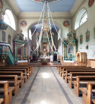 Zdjęcie nr 18: Kościół murowany, składa się z nawy i zwróconego na południe prezbiterium, do którego przylega zakrystia, nad którą znajduje się skarbiec; od północy wieża. Prezbiterium jest węższe od nawy, o zaokrąglonych narożach, oddzielone od prostokątnej nawy łukiem tęczowym. Ściany kościoła gładkie, przeprute półkolistymi oknami – dwoma w prezbiterium, sześcioma w nawie. Od zachodu chór wsparty na dwóch kolumnach, z balustradą wyłamaną na środku, dekorowaną u spodu lambrekinem. Ściany kościoła gładkie, w dolnej partii osłonięte drewnianą boazerią, z wnęką na chrzcielnicę po lewej i drugą na drzwi z prawej strony. Wnętrze przekrywają stropy – zwierciadlany w prezbiterium i płaski  z fasetami w nawie. Na nich oraz w górnej partii ścian polichromia. Nad prezbiterium wizerunek zmartwychwstałego Chrystusa, nad nawą zakomponowana w kole scena adoracji Najświętszej Marii Panny przez apostołów, poniżej, na ścianach medaliony z postaciami ważnych osobistości, świętych i aniołów. Główne drzwi od północy, boczne od zachodu. 
Kościół posadowiony na cokole. Elewacja frontowa ze zdwojonym ryzalitem, którego środek odpowiada szerokości wieży; podziały poziome przeprowadzone przy pomocy gzymsów. Na osi wejście i  okno, oba w boniowanym obramieniu. Okno ujmuje polichromowana scena Zwiastowania. Ryzalit wieńczy trójkątny fronton. Cofnięty ryzalit w dolnej partii boniowany, wyżej gładki, zwieńczony ćwierćkolistymi fragmentami przerwanego przyczółka. Boki elewacji frontowej gładkie, zwieńczone frontonem przerwanym na masyw czworobocznej wieży przeprutej z każdej strony oknem w kształcie stojącego prostokąta zamkniętego łukiem pełnym. Elewacje boczne gładkie, przeprute półkolistymi oknami. Od wschodu poniżej okien szare płyciny, od południa, w kapliczkowej oprawie grupa Ukrzyżowania. Dach nad nawą dwuspadowy, nad prezbiterium trójspadowy, dach wieńczy baniasty hełm z latarnią zakończony krzyżem, na kalenicy barokowa wieżyczka na sygnaturkę. 
