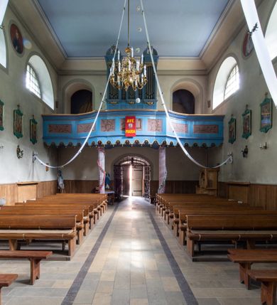 Zdjęcie nr 22: Kościół murowany, składa się z nawy i zwróconego na południe prezbiterium, do którego przylega zakrystia, nad którą znajduje się skarbiec; od północy wieża. Prezbiterium jest węższe od nawy, o zaokrąglonych narożach, oddzielone od prostokątnej nawy łukiem tęczowym. Ściany kościoła gładkie, przeprute półkolistymi oknami – dwoma w prezbiterium, sześcioma w nawie. Od zachodu chór wsparty na dwóch kolumnach, z balustradą wyłamaną na środku, dekorowaną u spodu lambrekinem. Ściany kościoła gładkie, w dolnej partii osłonięte drewnianą boazerią, z wnęką na chrzcielnicę po lewej i drugą na drzwi z prawej strony. Wnętrze przekrywają stropy – zwierciadlany w prezbiterium i płaski  z fasetami w nawie. Na nich oraz w górnej partii ścian polichromia. Nad prezbiterium wizerunek zmartwychwstałego Chrystusa, nad nawą zakomponowana w kole scena adoracji Najświętszej Marii Panny przez apostołów, poniżej, na ścianach medaliony z postaciami ważnych osobistości, świętych i aniołów. Główne drzwi od północy, boczne od zachodu. 
Kościół posadowiony na cokole. Elewacja frontowa ze zdwojonym ryzalitem, którego środek odpowiada szerokości wieży; podziały poziome przeprowadzone przy pomocy gzymsów. Na osi wejście i  okno, oba w boniowanym obramieniu. Okno ujmuje polichromowana scena Zwiastowania. Ryzalit wieńczy trójkątny fronton. Cofnięty ryzalit w dolnej partii boniowany, wyżej gładki, zwieńczony ćwierćkolistymi fragmentami przerwanego przyczółka. Boki elewacji frontowej gładkie, zwieńczone frontonem przerwanym na masyw czworobocznej wieży przeprutej z każdej strony oknem w kształcie stojącego prostokąta zamkniętego łukiem pełnym. Elewacje boczne gładkie, przeprute półkolistymi oknami. Od wschodu poniżej okien szare płyciny, od południa, w kapliczkowej oprawie grupa Ukrzyżowania. Dach nad nawą dwuspadowy, nad prezbiterium trójspadowy, dach wieńczy baniasty hełm z latarnią zakończony krzyżem, na kalenicy barokowa wieżyczka na sygnaturkę. 
