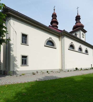 Zdjęcie nr 29: Kościół murowany, składa się z nawy i zwróconego na południe prezbiterium, do którego przylega zakrystia, nad którą znajduje się skarbiec; od północy wieża. Prezbiterium jest węższe od nawy, o zaokrąglonych narożach, oddzielone od prostokątnej nawy łukiem tęczowym. Ściany kościoła gładkie, przeprute półkolistymi oknami – dwoma w prezbiterium, sześcioma w nawie. Od zachodu chór wsparty na dwóch kolumnach, z balustradą wyłamaną na środku, dekorowaną u spodu lambrekinem. Ściany kościoła gładkie, w dolnej partii osłonięte drewnianą boazerią, z wnęką na chrzcielnicę po lewej i drugą na drzwi z prawej strony. Wnętrze przekrywają stropy – zwierciadlany w prezbiterium i płaski  z fasetami w nawie. Na nich oraz w górnej partii ścian polichromia. Nad prezbiterium wizerunek zmartwychwstałego Chrystusa, nad nawą zakomponowana w kole scena adoracji Najświętszej Marii Panny przez apostołów, poniżej, na ścianach medaliony z postaciami ważnych osobistości, świętych i aniołów. Główne drzwi od północy, boczne od zachodu. 
Kościół posadowiony na cokole. Elewacja frontowa ze zdwojonym ryzalitem, którego środek odpowiada szerokości wieży; podziały poziome przeprowadzone przy pomocy gzymsów. Na osi wejście i  okno, oba w boniowanym obramieniu. Okno ujmuje polichromowana scena Zwiastowania. Ryzalit wieńczy trójkątny fronton. Cofnięty ryzalit w dolnej partii boniowany, wyżej gładki, zwieńczony ćwierćkolistymi fragmentami przerwanego przyczółka. Boki elewacji frontowej gładkie, zwieńczone frontonem przerwanym na masyw czworobocznej wieży przeprutej z każdej strony oknem w kształcie stojącego prostokąta zamkniętego łukiem pełnym. Elewacje boczne gładkie, przeprute półkolistymi oknami. Od wschodu poniżej okien szare płyciny, od południa, w kapliczkowej oprawie grupa Ukrzyżowania. Dach nad nawą dwuspadowy, nad prezbiterium trójspadowy, dach wieńczy baniasty hełm z latarnią zakończony krzyżem, na kalenicy barokowa wieżyczka na sygnaturkę. 
