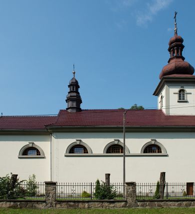 Zdjęcie nr 13: Kościół murowany, składa się z nawy i zwróconego na południe prezbiterium, do którego przylega zakrystia, nad którą znajduje się skarbiec; od północy wieża. Prezbiterium jest węższe od nawy, o zaokrąglonych narożach, oddzielone od prostokątnej nawy łukiem tęczowym. Ściany kościoła gładkie, przeprute półkolistymi oknami – dwoma w prezbiterium, sześcioma w nawie. Od zachodu chór wsparty na dwóch kolumnach, z balustradą wyłamaną na środku, dekorowaną u spodu lambrekinem. Ściany kościoła gładkie, w dolnej partii osłonięte drewnianą boazerią, z wnęką na chrzcielnicę po lewej i drugą na drzwi z prawej strony. Wnętrze przekrywają stropy – zwierciadlany w prezbiterium i płaski  z fasetami w nawie. Na nich oraz w górnej partii ścian polichromia. Nad prezbiterium wizerunek zmartwychwstałego Chrystusa, nad nawą zakomponowana w kole scena adoracji Najświętszej Marii Panny przez apostołów, poniżej, na ścianach medaliony z postaciami ważnych osobistości, świętych i aniołów. Główne drzwi od północy, boczne od zachodu. 
Kościół posadowiony na cokole. Elewacja frontowa ze zdwojonym ryzalitem, którego środek odpowiada szerokości wieży; podziały poziome przeprowadzone przy pomocy gzymsów. Na osi wejście i  okno, oba w boniowanym obramieniu. Okno ujmuje polichromowana scena Zwiastowania. Ryzalit wieńczy trójkątny fronton. Cofnięty ryzalit w dolnej partii boniowany, wyżej gładki, zwieńczony ćwierćkolistymi fragmentami przerwanego przyczółka. Boki elewacji frontowej gładkie, zwieńczone frontonem przerwanym na masyw czworobocznej wieży przeprutej z każdej strony oknem w kształcie stojącego prostokąta zamkniętego łukiem pełnym. Elewacje boczne gładkie, przeprute półkolistymi oknami. Od wschodu poniżej okien szare płyciny, od południa, w kapliczkowej oprawie grupa Ukrzyżowania. Dach nad nawą dwuspadowy, nad prezbiterium trójspadowy, dach wieńczy baniasty hełm z latarnią zakończony krzyżem, na kalenicy barokowa wieżyczka na sygnaturkę. 
