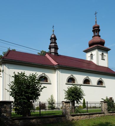 Zdjęcie nr 24: Kościół murowany, składa się z nawy i zwróconego na południe prezbiterium, do którego przylega zakrystia, nad którą znajduje się skarbiec; od północy wieża. Prezbiterium jest węższe od nawy, o zaokrąglonych narożach, oddzielone od prostokątnej nawy łukiem tęczowym. Ściany kościoła gładkie, przeprute półkolistymi oknami – dwoma w prezbiterium, sześcioma w nawie. Od zachodu chór wsparty na dwóch kolumnach, z balustradą wyłamaną na środku, dekorowaną u spodu lambrekinem. Ściany kościoła gładkie, w dolnej partii osłonięte drewnianą boazerią, z wnęką na chrzcielnicę po lewej i drugą na drzwi z prawej strony. Wnętrze przekrywają stropy – zwierciadlany w prezbiterium i płaski  z fasetami w nawie. Na nich oraz w górnej partii ścian polichromia. Nad prezbiterium wizerunek zmartwychwstałego Chrystusa, nad nawą zakomponowana w kole scena adoracji Najświętszej Marii Panny przez apostołów, poniżej, na ścianach medaliony z postaciami ważnych osobistości, świętych i aniołów. Główne drzwi od północy, boczne od zachodu. 
Kościół posadowiony na cokole. Elewacja frontowa ze zdwojonym ryzalitem, którego środek odpowiada szerokości wieży; podziały poziome przeprowadzone przy pomocy gzymsów. Na osi wejście i  okno, oba w boniowanym obramieniu. Okno ujmuje polichromowana scena Zwiastowania. Ryzalit wieńczy trójkątny fronton. Cofnięty ryzalit w dolnej partii boniowany, wyżej gładki, zwieńczony ćwierćkolistymi fragmentami przerwanego przyczółka. Boki elewacji frontowej gładkie, zwieńczone frontonem przerwanym na masyw czworobocznej wieży przeprutej z każdej strony oknem w kształcie stojącego prostokąta zamkniętego łukiem pełnym. Elewacje boczne gładkie, przeprute półkolistymi oknami. Od wschodu poniżej okien szare płyciny, od południa, w kapliczkowej oprawie grupa Ukrzyżowania. Dach nad nawą dwuspadowy, nad prezbiterium trójspadowy, dach wieńczy baniasty hełm z latarnią zakończony krzyżem, na kalenicy barokowa wieżyczka na sygnaturkę. 
