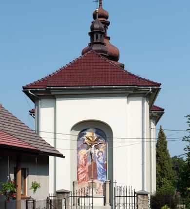 Zdjęcie nr 10: Kościół murowany, składa się z nawy i zwróconego na południe prezbiterium, do którego przylega zakrystia, nad którą znajduje się skarbiec; od północy wieża. Prezbiterium jest węższe od nawy, o zaokrąglonych narożach, oddzielone od prostokątnej nawy łukiem tęczowym. Ściany kościoła gładkie, przeprute półkolistymi oknami – dwoma w prezbiterium, sześcioma w nawie. Od zachodu chór wsparty na dwóch kolumnach, z balustradą wyłamaną na środku, dekorowaną u spodu lambrekinem. Ściany kościoła gładkie, w dolnej partii osłonięte drewnianą boazerią, z wnęką na chrzcielnicę po lewej i drugą na drzwi z prawej strony. Wnętrze przekrywają stropy – zwierciadlany w prezbiterium i płaski  z fasetami w nawie. Na nich oraz w górnej partii ścian polichromia. Nad prezbiterium wizerunek zmartwychwstałego Chrystusa, nad nawą zakomponowana w kole scena adoracji Najświętszej Marii Panny przez apostołów, poniżej, na ścianach medaliony z postaciami ważnych osobistości, świętych i aniołów. Główne drzwi od północy, boczne od zachodu. 
Kościół posadowiony na cokole. Elewacja frontowa ze zdwojonym ryzalitem, którego środek odpowiada szerokości wieży; podziały poziome przeprowadzone przy pomocy gzymsów. Na osi wejście i  okno, oba w boniowanym obramieniu. Okno ujmuje polichromowana scena Zwiastowania. Ryzalit wieńczy trójkątny fronton. Cofnięty ryzalit w dolnej partii boniowany, wyżej gładki, zwieńczony ćwierćkolistymi fragmentami przerwanego przyczółka. Boki elewacji frontowej gładkie, zwieńczone frontonem przerwanym na masyw czworobocznej wieży przeprutej z każdej strony oknem w kształcie stojącego prostokąta zamkniętego łukiem pełnym. Elewacje boczne gładkie, przeprute półkolistymi oknami. Od wschodu poniżej okien szare płyciny, od południa, w kapliczkowej oprawie grupa Ukrzyżowania. Dach nad nawą dwuspadowy, nad prezbiterium trójspadowy, dach wieńczy baniasty hełm z latarnią zakończony krzyżem, na kalenicy barokowa wieżyczka na sygnaturkę. 
