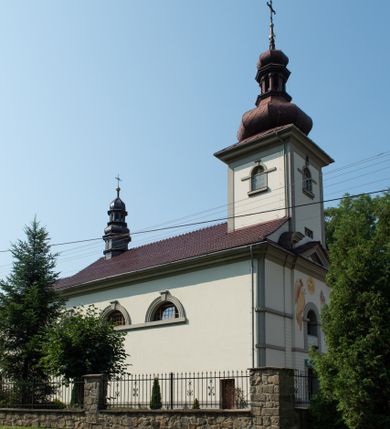 Zdjęcie nr 1: Kościół murowany, składa się z nawy i zwróconego na południe prezbiterium, do którego przylega zakrystia, nad którą znajduje się skarbiec; od północy wieża. Prezbiterium jest węższe od nawy, o zaokrąglonych narożach, oddzielone od prostokątnej nawy łukiem tęczowym. Ściany kościoła gładkie, przeprute półkolistymi oknami – dwoma w prezbiterium, sześcioma w nawie. Od zachodu chór wsparty na dwóch kolumnach, z balustradą wyłamaną na środku, dekorowaną u spodu lambrekinem. Ściany kościoła gładkie, w dolnej partii osłonięte drewnianą boazerią, z wnęką na chrzcielnicę po lewej i drugą na drzwi z prawej strony. Wnętrze przekrywają stropy – zwierciadlany w prezbiterium i płaski  z fasetami w nawie. Na nich oraz w górnej partii ścian polichromia. Nad prezbiterium wizerunek zmartwychwstałego Chrystusa, nad nawą zakomponowana w kole scena adoracji Najświętszej Marii Panny przez apostołów, poniżej, na ścianach medaliony z postaciami ważnych osobistości, świętych i aniołów. Główne drzwi od północy, boczne od zachodu. 
Kościół posadowiony na cokole. Elewacja frontowa ze zdwojonym ryzalitem, którego środek odpowiada szerokości wieży; podziały poziome przeprowadzone przy pomocy gzymsów. Na osi wejście i  okno, oba w boniowanym obramieniu. Okno ujmuje polichromowana scena Zwiastowania. Ryzalit wieńczy trójkątny fronton. Cofnięty ryzalit w dolnej partii boniowany, wyżej gładki, zwieńczony ćwierćkolistymi fragmentami przerwanego przyczółka. Boki elewacji frontowej gładkie, zwieńczone frontonem przerwanym na masyw czworobocznej wieży przeprutej z każdej strony oknem w kształcie stojącego prostokąta zamkniętego łukiem pełnym. Elewacje boczne gładkie, przeprute półkolistymi oknami. Od wschodu poniżej okien szare płyciny, od południa, w kapliczkowej oprawie grupa Ukrzyżowania. Dach nad nawą dwuspadowy, nad prezbiterium trójspadowy, dach wieńczy baniasty hełm z latarnią zakończony krzyżem, na kalenicy barokowa wieżyczka na sygnaturkę. 
