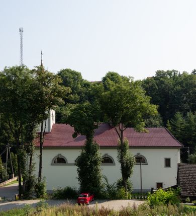 Zdjęcie nr 31: Kościół murowany, składa się z nawy i zwróconego na południe prezbiterium, do którego przylega zakrystia, nad którą znajduje się skarbiec; od północy wieża. Prezbiterium jest węższe od nawy, o zaokrąglonych narożach, oddzielone od prostokątnej nawy łukiem tęczowym. Ściany kościoła gładkie, przeprute półkolistymi oknami – dwoma w prezbiterium, sześcioma w nawie. Od zachodu chór wsparty na dwóch kolumnach, z balustradą wyłamaną na środku, dekorowaną u spodu lambrekinem. Ściany kościoła gładkie, w dolnej partii osłonięte drewnianą boazerią, z wnęką na chrzcielnicę po lewej i drugą na drzwi z prawej strony. Wnętrze przekrywają stropy – zwierciadlany w prezbiterium i płaski  z fasetami w nawie. Na nich oraz w górnej partii ścian polichromia. Nad prezbiterium wizerunek zmartwychwstałego Chrystusa, nad nawą zakomponowana w kole scena adoracji Najświętszej Marii Panny przez apostołów, poniżej, na ścianach medaliony z postaciami ważnych osobistości, świętych i aniołów. Główne drzwi od północy, boczne od zachodu. 
Kościół posadowiony na cokole. Elewacja frontowa ze zdwojonym ryzalitem, którego środek odpowiada szerokości wieży; podziały poziome przeprowadzone przy pomocy gzymsów. Na osi wejście i  okno, oba w boniowanym obramieniu. Okno ujmuje polichromowana scena Zwiastowania. Ryzalit wieńczy trójkątny fronton. Cofnięty ryzalit w dolnej partii boniowany, wyżej gładki, zwieńczony ćwierćkolistymi fragmentami przerwanego przyczółka. Boki elewacji frontowej gładkie, zwieńczone frontonem przerwanym na masyw czworobocznej wieży przeprutej z każdej strony oknem w kształcie stojącego prostokąta zamkniętego łukiem pełnym. Elewacje boczne gładkie, przeprute półkolistymi oknami. Od wschodu poniżej okien szare płyciny, od południa, w kapliczkowej oprawie grupa Ukrzyżowania. Dach nad nawą dwuspadowy, nad prezbiterium trójspadowy, dach wieńczy baniasty hełm z latarnią zakończony krzyżem, na kalenicy barokowa wieżyczka na sygnaturkę. 
