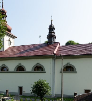 Zdjęcie nr 4: Kościół murowany, składa się z nawy i zwróconego na południe prezbiterium, do którego przylega zakrystia, nad którą znajduje się skarbiec; od północy wieża. Prezbiterium jest węższe od nawy, o zaokrąglonych narożach, oddzielone od prostokątnej nawy łukiem tęczowym. Ściany kościoła gładkie, przeprute półkolistymi oknami – dwoma w prezbiterium, sześcioma w nawie. Od zachodu chór wsparty na dwóch kolumnach, z balustradą wyłamaną na środku, dekorowaną u spodu lambrekinem. Ściany kościoła gładkie, w dolnej partii osłonięte drewnianą boazerią, z wnęką na chrzcielnicę po lewej i drugą na drzwi z prawej strony. Wnętrze przekrywają stropy – zwierciadlany w prezbiterium i płaski  z fasetami w nawie. Na nich oraz w górnej partii ścian polichromia. Nad prezbiterium wizerunek zmartwychwstałego Chrystusa, nad nawą zakomponowana w kole scena adoracji Najświętszej Marii Panny przez apostołów, poniżej, na ścianach medaliony z postaciami ważnych osobistości, świętych i aniołów. Główne drzwi od północy, boczne od zachodu. 
Kościół posadowiony na cokole. Elewacja frontowa ze zdwojonym ryzalitem, którego środek odpowiada szerokości wieży; podziały poziome przeprowadzone przy pomocy gzymsów. Na osi wejście i  okno, oba w boniowanym obramieniu. Okno ujmuje polichromowana scena Zwiastowania. Ryzalit wieńczy trójkątny fronton. Cofnięty ryzalit w dolnej partii boniowany, wyżej gładki, zwieńczony ćwierćkolistymi fragmentami przerwanego przyczółka. Boki elewacji frontowej gładkie, zwieńczone frontonem przerwanym na masyw czworobocznej wieży przeprutej z każdej strony oknem w kształcie stojącego prostokąta zamkniętego łukiem pełnym. Elewacje boczne gładkie, przeprute półkolistymi oknami. Od wschodu poniżej okien szare płyciny, od południa, w kapliczkowej oprawie grupa Ukrzyżowania. Dach nad nawą dwuspadowy, nad prezbiterium trójspadowy, dach wieńczy baniasty hełm z latarnią zakończony krzyżem, na kalenicy barokowa wieżyczka na sygnaturkę. 
