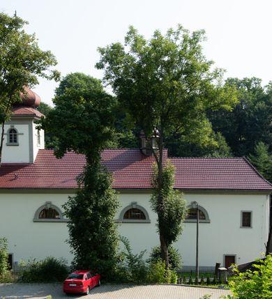 Zdjęcie nr 33: Kościół murowany, składa się z nawy i zwróconego na południe prezbiterium, do którego przylega zakrystia, nad którą znajduje się skarbiec; od północy wieża. Prezbiterium jest węższe od nawy, o zaokrąglonych narożach, oddzielone od prostokątnej nawy łukiem tęczowym. Ściany kościoła gładkie, przeprute półkolistymi oknami – dwoma w prezbiterium, sześcioma w nawie. Od zachodu chór wsparty na dwóch kolumnach, z balustradą wyłamaną na środku, dekorowaną u spodu lambrekinem. Ściany kościoła gładkie, w dolnej partii osłonięte drewnianą boazerią, z wnęką na chrzcielnicę po lewej i drugą na drzwi z prawej strony. Wnętrze przekrywają stropy – zwierciadlany w prezbiterium i płaski  z fasetami w nawie. Na nich oraz w górnej partii ścian polichromia. Nad prezbiterium wizerunek zmartwychwstałego Chrystusa, nad nawą zakomponowana w kole scena adoracji Najświętszej Marii Panny przez apostołów, poniżej, na ścianach medaliony z postaciami ważnych osobistości, świętych i aniołów. Główne drzwi od północy, boczne od zachodu. 
Kościół posadowiony na cokole. Elewacja frontowa ze zdwojonym ryzalitem, którego środek odpowiada szerokości wieży; podziały poziome przeprowadzone przy pomocy gzymsów. Na osi wejście i  okno, oba w boniowanym obramieniu. Okno ujmuje polichromowana scena Zwiastowania. Ryzalit wieńczy trójkątny fronton. Cofnięty ryzalit w dolnej partii boniowany, wyżej gładki, zwieńczony ćwierćkolistymi fragmentami przerwanego przyczółka. Boki elewacji frontowej gładkie, zwieńczone frontonem przerwanym na masyw czworobocznej wieży przeprutej z każdej strony oknem w kształcie stojącego prostokąta zamkniętego łukiem pełnym. Elewacje boczne gładkie, przeprute półkolistymi oknami. Od wschodu poniżej okien szare płyciny, od południa, w kapliczkowej oprawie grupa Ukrzyżowania. Dach nad nawą dwuspadowy, nad prezbiterium trójspadowy, dach wieńczy baniasty hełm z latarnią zakończony krzyżem, na kalenicy barokowa wieżyczka na sygnaturkę. 
