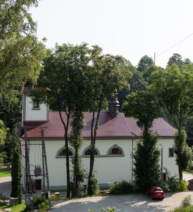 Zdjęcie nr 32: Kościół murowany, składa się z nawy i zwróconego na południe prezbiterium, do którego przylega zakrystia, nad którą znajduje się skarbiec; od północy wieża. Prezbiterium jest węższe od nawy, o zaokrąglonych narożach, oddzielone od prostokątnej nawy łukiem tęczowym. Ściany kościoła gładkie, przeprute półkolistymi oknami – dwoma w prezbiterium, sześcioma w nawie. Od zachodu chór wsparty na dwóch kolumnach, z balustradą wyłamaną na środku, dekorowaną u spodu lambrekinem. Ściany kościoła gładkie, w dolnej partii osłonięte drewnianą boazerią, z wnęką na chrzcielnicę po lewej i drugą na drzwi z prawej strony. Wnętrze przekrywają stropy – zwierciadlany w prezbiterium i płaski  z fasetami w nawie. Na nich oraz w górnej partii ścian polichromia. Nad prezbiterium wizerunek zmartwychwstałego Chrystusa, nad nawą zakomponowana w kole scena adoracji Najświętszej Marii Panny przez apostołów, poniżej, na ścianach medaliony z postaciami ważnych osobistości, świętych i aniołów. Główne drzwi od północy, boczne od zachodu. 
Kościół posadowiony na cokole. Elewacja frontowa ze zdwojonym ryzalitem, którego środek odpowiada szerokości wieży; podziały poziome przeprowadzone przy pomocy gzymsów. Na osi wejście i  okno, oba w boniowanym obramieniu. Okno ujmuje polichromowana scena Zwiastowania. Ryzalit wieńczy trójkątny fronton. Cofnięty ryzalit w dolnej partii boniowany, wyżej gładki, zwieńczony ćwierćkolistymi fragmentami przerwanego przyczółka. Boki elewacji frontowej gładkie, zwieńczone frontonem przerwanym na masyw czworobocznej wieży przeprutej z każdej strony oknem w kształcie stojącego prostokąta zamkniętego łukiem pełnym. Elewacje boczne gładkie, przeprute półkolistymi oknami. Od wschodu poniżej okien szare płyciny, od południa, w kapliczkowej oprawie grupa Ukrzyżowania. Dach nad nawą dwuspadowy, nad prezbiterium trójspadowy, dach wieńczy baniasty hełm z latarnią zakończony krzyżem, na kalenicy barokowa wieżyczka na sygnaturkę. 
