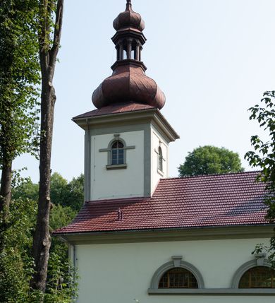 Zdjęcie nr 5: Kościół murowany, składa się z nawy i zwróconego na południe prezbiterium, do którego przylega zakrystia, nad którą znajduje się skarbiec; od północy wieża. Prezbiterium jest węższe od nawy, o zaokrąglonych narożach, oddzielone od prostokątnej nawy łukiem tęczowym. Ściany kościoła gładkie, przeprute półkolistymi oknami – dwoma w prezbiterium, sześcioma w nawie. Od zachodu chór wsparty na dwóch kolumnach, z balustradą wyłamaną na środku, dekorowaną u spodu lambrekinem. Ściany kościoła gładkie, w dolnej partii osłonięte drewnianą boazerią, z wnęką na chrzcielnicę po lewej i drugą na drzwi z prawej strony. Wnętrze przekrywają stropy – zwierciadlany w prezbiterium i płaski  z fasetami w nawie. Na nich oraz w górnej partii ścian polichromia. Nad prezbiterium wizerunek zmartwychwstałego Chrystusa, nad nawą zakomponowana w kole scena adoracji Najświętszej Marii Panny przez apostołów, poniżej, na ścianach medaliony z postaciami ważnych osobistości, świętych i aniołów. Główne drzwi od północy, boczne od zachodu. 
Kościół posadowiony na cokole. Elewacja frontowa ze zdwojonym ryzalitem, którego środek odpowiada szerokości wieży; podziały poziome przeprowadzone przy pomocy gzymsów. Na osi wejście i  okno, oba w boniowanym obramieniu. Okno ujmuje polichromowana scena Zwiastowania. Ryzalit wieńczy trójkątny fronton. Cofnięty ryzalit w dolnej partii boniowany, wyżej gładki, zwieńczony ćwierćkolistymi fragmentami przerwanego przyczółka. Boki elewacji frontowej gładkie, zwieńczone frontonem przerwanym na masyw czworobocznej wieży przeprutej z każdej strony oknem w kształcie stojącego prostokąta zamkniętego łukiem pełnym. Elewacje boczne gładkie, przeprute półkolistymi oknami. Od wschodu poniżej okien szare płyciny, od południa, w kapliczkowej oprawie grupa Ukrzyżowania. Dach nad nawą dwuspadowy, nad prezbiterium trójspadowy, dach wieńczy baniasty hełm z latarnią zakończony krzyżem, na kalenicy barokowa wieżyczka na sygnaturkę. 
