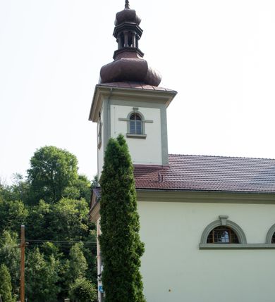 Zdjęcie nr 6: Kościół murowany, składa się z nawy i zwróconego na południe prezbiterium, do którego przylega zakrystia, nad którą znajduje się skarbiec; od północy wieża. Prezbiterium jest węższe od nawy, o zaokrąglonych narożach, oddzielone od prostokątnej nawy łukiem tęczowym. Ściany kościoła gładkie, przeprute półkolistymi oknami – dwoma w prezbiterium, sześcioma w nawie. Od zachodu chór wsparty na dwóch kolumnach, z balustradą wyłamaną na środku, dekorowaną u spodu lambrekinem. Ściany kościoła gładkie, w dolnej partii osłonięte drewnianą boazerią, z wnęką na chrzcielnicę po lewej i drugą na drzwi z prawej strony. Wnętrze przekrywają stropy – zwierciadlany w prezbiterium i płaski  z fasetami w nawie. Na nich oraz w górnej partii ścian polichromia. Nad prezbiterium wizerunek zmartwychwstałego Chrystusa, nad nawą zakomponowana w kole scena adoracji Najświętszej Marii Panny przez apostołów, poniżej, na ścianach medaliony z postaciami ważnych osobistości, świętych i aniołów. Główne drzwi od północy, boczne od zachodu. 
Kościół posadowiony na cokole. Elewacja frontowa ze zdwojonym ryzalitem, którego środek odpowiada szerokości wieży; podziały poziome przeprowadzone przy pomocy gzymsów. Na osi wejście i  okno, oba w boniowanym obramieniu. Okno ujmuje polichromowana scena Zwiastowania. Ryzalit wieńczy trójkątny fronton. Cofnięty ryzalit w dolnej partii boniowany, wyżej gładki, zwieńczony ćwierćkolistymi fragmentami przerwanego przyczółka. Boki elewacji frontowej gładkie, zwieńczone frontonem przerwanym na masyw czworobocznej wieży przeprutej z każdej strony oknem w kształcie stojącego prostokąta zamkniętego łukiem pełnym. Elewacje boczne gładkie, przeprute półkolistymi oknami. Od wschodu poniżej okien szare płyciny, od południa, w kapliczkowej oprawie grupa Ukrzyżowania. Dach nad nawą dwuspadowy, nad prezbiterium trójspadowy, dach wieńczy baniasty hełm z latarnią zakończony krzyżem, na kalenicy barokowa wieżyczka na sygnaturkę. 
