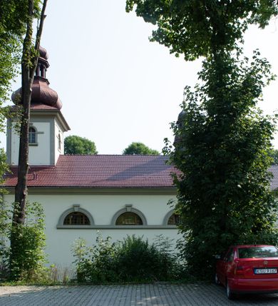 Zdjęcie nr 34: Kościół murowany, składa się z nawy i zwróconego na południe prezbiterium, do którego przylega zakrystia, nad którą znajduje się skarbiec; od północy wieża. Prezbiterium jest węższe od nawy, o zaokrąglonych narożach, oddzielone od prostokątnej nawy łukiem tęczowym. Ściany kościoła gładkie, przeprute półkolistymi oknami – dwoma w prezbiterium, sześcioma w nawie. Od zachodu chór wsparty na dwóch kolumnach, z balustradą wyłamaną na środku, dekorowaną u spodu lambrekinem. Ściany kościoła gładkie, w dolnej partii osłonięte drewnianą boazerią, z wnęką na chrzcielnicę po lewej i drugą na drzwi z prawej strony. Wnętrze przekrywają stropy – zwierciadlany w prezbiterium i płaski  z fasetami w nawie. Na nich oraz w górnej partii ścian polichromia. Nad prezbiterium wizerunek zmartwychwstałego Chrystusa, nad nawą zakomponowana w kole scena adoracji Najświętszej Marii Panny przez apostołów, poniżej, na ścianach medaliony z postaciami ważnych osobistości, świętych i aniołów. Główne drzwi od północy, boczne od zachodu. 
Kościół posadowiony na cokole. Elewacja frontowa ze zdwojonym ryzalitem, którego środek odpowiada szerokości wieży; podziały poziome przeprowadzone przy pomocy gzymsów. Na osi wejście i  okno, oba w boniowanym obramieniu. Okno ujmuje polichromowana scena Zwiastowania. Ryzalit wieńczy trójkątny fronton. Cofnięty ryzalit w dolnej partii boniowany, wyżej gładki, zwieńczony ćwierćkolistymi fragmentami przerwanego przyczółka. Boki elewacji frontowej gładkie, zwieńczone frontonem przerwanym na masyw czworobocznej wieży przeprutej z każdej strony oknem w kształcie stojącego prostokąta zamkniętego łukiem pełnym. Elewacje boczne gładkie, przeprute półkolistymi oknami. Od wschodu poniżej okien szare płyciny, od południa, w kapliczkowej oprawie grupa Ukrzyżowania. Dach nad nawą dwuspadowy, nad prezbiterium trójspadowy, dach wieńczy baniasty hełm z latarnią zakończony krzyżem, na kalenicy barokowa wieżyczka na sygnaturkę. 
