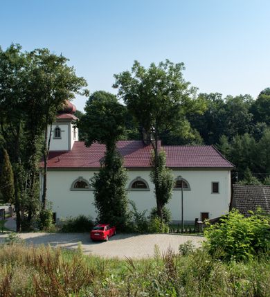 Zdjęcie nr 30: Kościół murowany, składa się z nawy i zwróconego na południe prezbiterium, do którego przylega zakrystia, nad którą znajduje się skarbiec; od północy wieża. Prezbiterium jest węższe od nawy, o zaokrąglonych narożach, oddzielone od prostokątnej nawy łukiem tęczowym. Ściany kościoła gładkie, przeprute półkolistymi oknami – dwoma w prezbiterium, sześcioma w nawie. Od zachodu chór wsparty na dwóch kolumnach, z balustradą wyłamaną na środku, dekorowaną u spodu lambrekinem. Ściany kościoła gładkie, w dolnej partii osłonięte drewnianą boazerią, z wnęką na chrzcielnicę po lewej i drugą na drzwi z prawej strony. Wnętrze przekrywają stropy – zwierciadlany w prezbiterium i płaski  z fasetami w nawie. Na nich oraz w górnej partii ścian polichromia. Nad prezbiterium wizerunek zmartwychwstałego Chrystusa, nad nawą zakomponowana w kole scena adoracji Najświętszej Marii Panny przez apostołów, poniżej, na ścianach medaliony z postaciami ważnych osobistości, świętych i aniołów. Główne drzwi od północy, boczne od zachodu. 
Kościół posadowiony na cokole. Elewacja frontowa ze zdwojonym ryzalitem, którego środek odpowiada szerokości wieży; podziały poziome przeprowadzone przy pomocy gzymsów. Na osi wejście i  okno, oba w boniowanym obramieniu. Okno ujmuje polichromowana scena Zwiastowania. Ryzalit wieńczy trójkątny fronton. Cofnięty ryzalit w dolnej partii boniowany, wyżej gładki, zwieńczony ćwierćkolistymi fragmentami przerwanego przyczółka. Boki elewacji frontowej gładkie, zwieńczone frontonem przerwanym na masyw czworobocznej wieży przeprutej z każdej strony oknem w kształcie stojącego prostokąta zamkniętego łukiem pełnym. Elewacje boczne gładkie, przeprute półkolistymi oknami. Od wschodu poniżej okien szare płyciny, od południa, w kapliczkowej oprawie grupa Ukrzyżowania. Dach nad nawą dwuspadowy, nad prezbiterium trójspadowy, dach wieńczy baniasty hełm z latarnią zakończony krzyżem, na kalenicy barokowa wieżyczka na sygnaturkę. 
