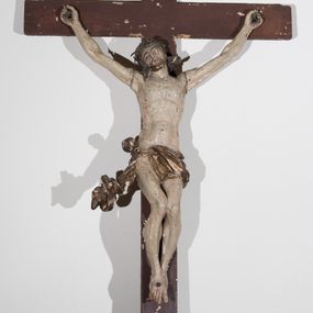 Zdjęcie nr 1: Krzyż o prostym zakończeniu ramion, ustawiony na wklęsło-wypukłej podstawie z muszlą, przytwierdzonej do drążka. Figura żywego Chrystusa przybita do krzyża trzema gwoździami. Ciało w dużym zwisie, o łukowatym układzie ramion, głowie przechylonej w prawo, esowato wygiętej sylwetce, nogi ma ugięte, a stopy skrzyżowane w układzie prawa na lewą. Chrystus ma owalną twarz, o półprzymkniętych oczach, prostym nosie i otwartych ustach, okoloną krótką brodą i silnie kręconymi, rozwianymi włosami sięgającymi ramion. Na głowie ma koronę cierniową. Ciało szczupłe, o delikatnie podkreślonej muskulaturze klatki piersiowej i z wyraźnie zaznaczonymi mięśniami ramion i nóg. Perizonium złocone, krótkie, zawieszone na podwójnym sznurze, odsłaniające prawe udo, przesłaniające partie podbrzusza i lewe biodro, o silnie rozwianym zwisie tkaniny przy prawym boku. Polichromia ciała naturalistyczna z zaznaczonymi śladami męki. Na zwieńczeniu pionowej belki krzyża srebrzona banderola z napisem „I.N.R.I.”.