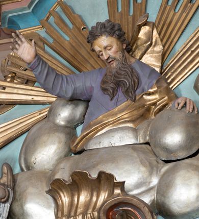 Zdjęcie nr 14: Nastawa ołtarzowa architektoniczna, jednoosiowa, jednokondygnacyjna ze zwieńczeniem, ustawiona na dwustrefowym cokole, z wyodrębnionymi dwiema parami prostopadłościanów. Ołtarz kamienny, wolnostojący, ustawiony na dwustopniowej podstawie, ujęty po bokach fryzowanymi konsolami. Mensa kamienna z marmurowym portatylem. Na przedniej ściance wyrzeźbiona w licu płycina, ujęta kanelowanymi lizenami, z monogramem IHS w polu. Na ołtarzu ustawione tabernakulum z tronem wystawienia. Tabernakulum w formie drewnianej skrzynki z obitymi blachą prostokątnymi drzwiczkami, ujętymi ramą. W ich polu medalion z przedstawieniem pelikana karmiącego młode na tle krzyża. Tron wystawienia w formie obrotowej, trójdzielnej niszy o wykroju stojącego prostokąta zamkniętego stylizowanym łukiem półokrągłym, zwieńczonej gzymsem. Nisza flankowana dekoracją w postaci liści ostrokrzewu i kampanuli, na gzymsie rocaille. Tabernakulum i tron ujęte parą niższych kolumn o kapitelach kompozytowych, na wysokich cokołach, dźwigających imposty, na których stoją wazony oraz spływami zakończonymi cokołami z fragmentami przerwanego przyczółka, na których klęczą adorujące anioły. Spływy dekorowane rocaille&#039;em z podwieszonymi kampanulami. Kondygnacja ujęta dwiema parami pilastrów i stojących przed nimi kolumn o kapitelach kompozytowych, ustawionymi delikatnie pod kątem względem lica, wewnętrzna para wysunięta do przodu. Po wewnętrznej stronie ołtarza para pilastrów, których konsole podtrzymują belkowanie, a trzony dekorowane są zwisami roślinnymi, na ich tle figury św. Joachima i św. Anny. Podpory dźwigają pełne belkowanie, wyłamane na ich osi, przerwane nad polem środkowym oraz fragmenty przerwanego, falistego przyczółka z siedzącymi puttami, a także wolutowe cokoły z wazonami na zewnętrznych krawędziach belkowania. Fryz dekorowany rozetami. W polu środkowym nisza w formie stojącego prostokąta zamkniętego łukiem półkolistym nadwieszonym, ujęta profilowaną ramą z mniejszym obrazem Matki Boskiej z Dzieciątkiem oraz przedstawieniem św. Klemensa na zasuwie. Powyżej rokokowy kartusz z monogramem Marii, na którym dwa putta trzymają koronę, z podwieszonymi zwisami kwiatowymi, ujmującymi ramę pola głównego poniżej. Zwieńczenie w formie stojącego prostokąta z wolutowymi uszakami, zamkniętego gzymsem w formie łuku odcinkowego nadwieszonego. W polu rzeźbiarskie przedstawienie półpostaci Boga Ojca pośród obłoków, na tle glorii promienistej, ujętego przez siedzące na gzymsie, adorujące aniołki. Ołtarz flankują umocowane do ścian konsole z figurami św. Piotra i św. Pawła. Struktura w całości polichromowana w kolorze jasnoniebieskim, z niebieskimi i bladoróżowymi detalami, kolumny, profile i ornamentyka złocone, detale srebrzone.  
