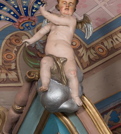 Zdjęcie nr 17: Nastawa ołtarzowa architektoniczna, jednoosiowa, jednokondygnacyjna ze zwieńczeniem, ustawiona na dwustrefowym cokole, z wyodrębnionymi dwiema parami prostopadłościanów. Ołtarz kamienny, wolnostojący, ustawiony na dwustopniowej podstawie, ujęty po bokach fryzowanymi konsolami. Mensa kamienna z marmurowym portatylem. Na przedniej ściance wyrzeźbiona w licu płycina, ujęta kanelowanymi lizenami, z monogramem IHS w polu. Na ołtarzu ustawione tabernakulum z tronem wystawienia. Tabernakulum w formie drewnianej skrzynki z obitymi blachą prostokątnymi drzwiczkami, ujętymi ramą. W ich polu medalion z przedstawieniem pelikana karmiącego młode na tle krzyża. Tron wystawienia w formie obrotowej, trójdzielnej niszy o wykroju stojącego prostokąta zamkniętego stylizowanym łukiem półokrągłym, zwieńczonej gzymsem. Nisza flankowana dekoracją w postaci liści ostrokrzewu i kampanuli, na gzymsie rocaille. Tabernakulum i tron ujęte parą niższych kolumn o kapitelach kompozytowych, na wysokich cokołach, dźwigających imposty, na których stoją wazony oraz spływami zakończonymi cokołami z fragmentami przerwanego przyczółka, na których klęczą adorujące anioły. Spływy dekorowane rocaille'em z podwieszonymi kampanulami. Kondygnacja ujęta dwiema parami pilastrów i stojących przed nimi kolumn o kapitelach kompozytowych, ustawionymi delikatnie pod kątem względem lica, wewnętrzna para wysunięta do przodu. Po wewnętrznej stronie ołtarza para pilastrów, których konsole podtrzymują belkowanie, a trzony dekorowane są zwisami roślinnymi, na ich tle figury św. Joachima i św. Anny. Podpory dźwigają pełne belkowanie, wyłamane na ich osi, przerwane nad polem środkowym oraz fragmenty przerwanego, falistego przyczółka z siedzącymi puttami, a także wolutowe cokoły z wazonami na zewnętrznych krawędziach belkowania. Fryz dekorowany rozetami. W polu środkowym nisza w formie stojącego prostokąta zamkniętego łukiem półkolistym nadwieszonym, ujęta profilowaną ramą z mniejszym obrazem Matki Boskiej z Dzieciątkiem oraz przedstawieniem św. Klemensa na zasuwie. Powyżej rokokowy kartusz z monogramem Marii, na którym dwa putta trzymają koronę, z podwieszonymi zwisami kwiatowymi, ujmującymi ramę pola głównego poniżej. Zwieńczenie w formie stojącego prostokąta z wolutowymi uszakami, zamkniętego gzymsem w formie łuku odcinkowego nadwieszonego. W polu rzeźbiarskie przedstawienie półpostaci Boga Ojca pośród obłoków, na tle glorii promienistej, ujętego przez siedzące na gzymsie, adorujące aniołki. Ołtarz flankują umocowane do ścian konsole z figurami św. Piotra i św. Pawła. Struktura w całości polichromowana w kolorze jasnoniebieskim, z niebieskimi i bladoróżowymi detalami, kolumny, profile i ornamentyka złocone, detale srebrzone.  
