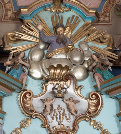 Zdjęcie nr 11: Nastawa ołtarzowa architektoniczna, jednoosiowa, jednokondygnacyjna ze zwieńczeniem, ustawiona na dwustrefowym cokole, z wyodrębnionymi dwiema parami prostopadłościanów. Ołtarz kamienny, wolnostojący, ustawiony na dwustopniowej podstawie, ujęty po bokach fryzowanymi konsolami. Mensa kamienna z marmurowym portatylem. Na przedniej ściance wyrzeźbiona w licu płycina, ujęta kanelowanymi lizenami, z monogramem IHS w polu. Na ołtarzu ustawione tabernakulum z tronem wystawienia. Tabernakulum w formie drewnianej skrzynki z obitymi blachą prostokątnymi drzwiczkami, ujętymi ramą. W ich polu medalion z przedstawieniem pelikana karmiącego młode na tle krzyża. Tron wystawienia w formie obrotowej, trójdzielnej niszy o wykroju stojącego prostokąta zamkniętego stylizowanym łukiem półokrągłym, zwieńczonej gzymsem. Nisza flankowana dekoracją w postaci liści ostrokrzewu i kampanuli, na gzymsie rocaille. Tabernakulum i tron ujęte parą niższych kolumn o kapitelach kompozytowych, na wysokich cokołach, dźwigających imposty, na których stoją wazony oraz spływami zakończonymi cokołami z fragmentami przerwanego przyczółka, na których klęczą adorujące anioły. Spływy dekorowane rocaille'em z podwieszonymi kampanulami. Kondygnacja ujęta dwiema parami pilastrów i stojących przed nimi kolumn o kapitelach kompozytowych, ustawionymi delikatnie pod kątem względem lica, wewnętrzna para wysunięta do przodu. Po wewnętrznej stronie ołtarza para pilastrów, których konsole podtrzymują belkowanie, a trzony dekorowane są zwisami roślinnymi, na ich tle figury św. Joachima i św. Anny. Podpory dźwigają pełne belkowanie, wyłamane na ich osi, przerwane nad polem środkowym oraz fragmenty przerwanego, falistego przyczółka z siedzącymi puttami, a także wolutowe cokoły z wazonami na zewnętrznych krawędziach belkowania. Fryz dekorowany rozetami. W polu środkowym nisza w formie stojącego prostokąta zamkniętego łukiem półkolistym nadwieszonym, ujęta profilowaną ramą z mniejszym obrazem Matki Boskiej z Dzieciątkiem oraz przedstawieniem św. Klemensa na zasuwie. Powyżej rokokowy kartusz z monogramem Marii, na którym dwa putta trzymają koronę, z podwieszonymi zwisami kwiatowymi, ujmującymi ramę pola głównego poniżej. Zwieńczenie w formie stojącego prostokąta z wolutowymi uszakami, zamkniętego gzymsem w formie łuku odcinkowego nadwieszonego. W polu rzeźbiarskie przedstawienie półpostaci Boga Ojca pośród obłoków, na tle glorii promienistej, ujętego przez siedzące na gzymsie, adorujące aniołki. Ołtarz flankują umocowane do ścian konsole z figurami św. Piotra i św. Pawła. Struktura w całości polichromowana w kolorze jasnoniebieskim, z niebieskimi i bladoróżowymi detalami, kolumny, profile i ornamentyka złocone, detale srebrzone.  
