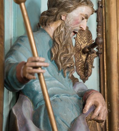 Zdjęcie nr 20: Nastawa ołtarzowa architektoniczna, jednoosiowa, jednokondygnacyjna ze zwieńczeniem, ustawiona na dwustrefowym cokole, z wyodrębnionymi dwiema parami prostopadłościanów. Ołtarz kamienny, wolnostojący, ustawiony na dwustopniowej podstawie, ujęty po bokach fryzowanymi konsolami. Mensa kamienna z marmurowym portatylem. Na przedniej ściance wyrzeźbiona w licu płycina, ujęta kanelowanymi lizenami, z monogramem IHS w polu. Na ołtarzu ustawione tabernakulum z tronem wystawienia. Tabernakulum w formie drewnianej skrzynki z obitymi blachą prostokątnymi drzwiczkami, ujętymi ramą. W ich polu medalion z przedstawieniem pelikana karmiącego młode na tle krzyża. Tron wystawienia w formie obrotowej, trójdzielnej niszy o wykroju stojącego prostokąta zamkniętego stylizowanym łukiem półokrągłym, zwieńczonej gzymsem. Nisza flankowana dekoracją w postaci liści ostrokrzewu i kampanuli, na gzymsie rocaille. Tabernakulum i tron ujęte parą niższych kolumn o kapitelach kompozytowych, na wysokich cokołach, dźwigających imposty, na których stoją wazony oraz spływami zakończonymi cokołami z fragmentami przerwanego przyczółka, na których klęczą adorujące anioły. Spływy dekorowane rocaille'em z podwieszonymi kampanulami. Kondygnacja ujęta dwiema parami pilastrów i stojących przed nimi kolumn o kapitelach kompozytowych, ustawionymi delikatnie pod kątem względem lica, wewnętrzna para wysunięta do przodu. Po wewnętrznej stronie ołtarza para pilastrów, których konsole podtrzymują belkowanie, a trzony dekorowane są zwisami roślinnymi, na ich tle figury św. Joachima i św. Anny. Podpory dźwigają pełne belkowanie, wyłamane na ich osi, przerwane nad polem środkowym oraz fragmenty przerwanego, falistego przyczółka z siedzącymi puttami, a także wolutowe cokoły z wazonami na zewnętrznych krawędziach belkowania. Fryz dekorowany rozetami. W polu środkowym nisza w formie stojącego prostokąta zamkniętego łukiem półkolistym nadwieszonym, ujęta profilowaną ramą z mniejszym obrazem Matki Boskiej z Dzieciątkiem oraz przedstawieniem św. Klemensa na zasuwie. Powyżej rokokowy kartusz z monogramem Marii, na którym dwa putta trzymają koronę, z podwieszonymi zwisami kwiatowymi, ujmującymi ramę pola głównego poniżej. Zwieńczenie w formie stojącego prostokąta z wolutowymi uszakami, zamkniętego gzymsem w formie łuku odcinkowego nadwieszonego. W polu rzeźbiarskie przedstawienie półpostaci Boga Ojca pośród obłoków, na tle glorii promienistej, ujętego przez siedzące na gzymsie, adorujące aniołki. Ołtarz flankują umocowane do ścian konsole z figurami św. Piotra i św. Pawła. Struktura w całości polichromowana w kolorze jasnoniebieskim, z niebieskimi i bladoróżowymi detalami, kolumny, profile i ornamentyka złocone, detale srebrzone.  
