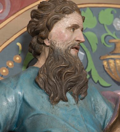 Zdjęcie nr 26: Nastawa ołtarzowa architektoniczna, jednoosiowa, jednokondygnacyjna ze zwieńczeniem, ustawiona na dwustrefowym cokole, z wyodrębnionymi dwiema parami prostopadłościanów. Ołtarz kamienny, wolnostojący, ustawiony na dwustopniowej podstawie, ujęty po bokach fryzowanymi konsolami. Mensa kamienna z marmurowym portatylem. Na przedniej ściance wyrzeźbiona w licu płycina, ujęta kanelowanymi lizenami, z monogramem IHS w polu. Na ołtarzu ustawione tabernakulum z tronem wystawienia. Tabernakulum w formie drewnianej skrzynki z obitymi blachą prostokątnymi drzwiczkami, ujętymi ramą. W ich polu medalion z przedstawieniem pelikana karmiącego młode na tle krzyża. Tron wystawienia w formie obrotowej, trójdzielnej niszy o wykroju stojącego prostokąta zamkniętego stylizowanym łukiem półokrągłym, zwieńczonej gzymsem. Nisza flankowana dekoracją w postaci liści ostrokrzewu i kampanuli, na gzymsie rocaille. Tabernakulum i tron ujęte parą niższych kolumn o kapitelach kompozytowych, na wysokich cokołach, dźwigających imposty, na których stoją wazony oraz spływami zakończonymi cokołami z fragmentami przerwanego przyczółka, na których klęczą adorujące anioły. Spływy dekorowane rocaille'em z podwieszonymi kampanulami. Kondygnacja ujęta dwiema parami pilastrów i stojących przed nimi kolumn o kapitelach kompozytowych, ustawionymi delikatnie pod kątem względem lica, wewnętrzna para wysunięta do przodu. Po wewnętrznej stronie ołtarza para pilastrów, których konsole podtrzymują belkowanie, a trzony dekorowane są zwisami roślinnymi, na ich tle figury św. Joachima i św. Anny. Podpory dźwigają pełne belkowanie, wyłamane na ich osi, przerwane nad polem środkowym oraz fragmenty przerwanego, falistego przyczółka z siedzącymi puttami, a także wolutowe cokoły z wazonami na zewnętrznych krawędziach belkowania. Fryz dekorowany rozetami. W polu środkowym nisza w formie stojącego prostokąta zamkniętego łukiem półkolistym nadwieszonym, ujęta profilowaną ramą z mniejszym obrazem Matki Boskiej z Dzieciątkiem oraz przedstawieniem św. Klemensa na zasuwie. Powyżej rokokowy kartusz z monogramem Marii, na którym dwa putta trzymają koronę, z podwieszonymi zwisami kwiatowymi, ujmującymi ramę pola głównego poniżej. Zwieńczenie w formie stojącego prostokąta z wolutowymi uszakami, zamkniętego gzymsem w formie łuku odcinkowego nadwieszonego. W polu rzeźbiarskie przedstawienie półpostaci Boga Ojca pośród obłoków, na tle glorii promienistej, ujętego przez siedzące na gzymsie, adorujące aniołki. Ołtarz flankują umocowane do ścian konsole z figurami św. Piotra i św. Pawła. Struktura w całości polichromowana w kolorze jasnoniebieskim, z niebieskimi i bladoróżowymi detalami, kolumny, profile i ornamentyka złocone, detale srebrzone.  
