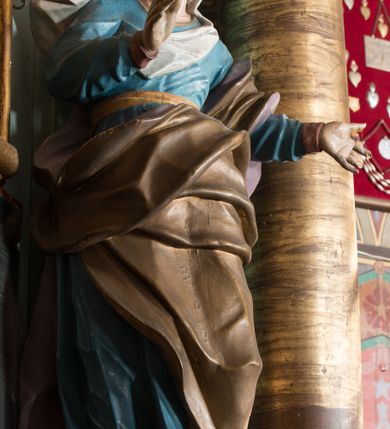 Zdjęcie nr 33: Nastawa ołtarzowa architektoniczna, jednoosiowa, jednokondygnacyjna ze zwieńczeniem, ustawiona na dwustrefowym cokole, z wyodrębnionymi dwiema parami prostopadłościanów. Ołtarz kamienny, wolnostojący, ustawiony na dwustopniowej podstawie, ujęty po bokach fryzowanymi konsolami. Mensa kamienna z marmurowym portatylem. Na przedniej ściance wyrzeźbiona w licu płycina, ujęta kanelowanymi lizenami, z monogramem IHS w polu. Na ołtarzu ustawione tabernakulum z tronem wystawienia. Tabernakulum w formie drewnianej skrzynki z obitymi blachą prostokątnymi drzwiczkami, ujętymi ramą. W ich polu medalion z przedstawieniem pelikana karmiącego młode na tle krzyża. Tron wystawienia w formie obrotowej, trójdzielnej niszy o wykroju stojącego prostokąta zamkniętego stylizowanym łukiem półokrągłym, zwieńczonej gzymsem. Nisza flankowana dekoracją w postaci liści ostrokrzewu i kampanuli, na gzymsie rocaille. Tabernakulum i tron ujęte parą niższych kolumn o kapitelach kompozytowych, na wysokich cokołach, dźwigających imposty, na których stoją wazony oraz spływami zakończonymi cokołami z fragmentami przerwanego przyczółka, na których klęczą adorujące anioły. Spływy dekorowane rocaille'em z podwieszonymi kampanulami. Kondygnacja ujęta dwiema parami pilastrów i stojących przed nimi kolumn o kapitelach kompozytowych, ustawionymi delikatnie pod kątem względem lica, wewnętrzna para wysunięta do przodu. Po wewnętrznej stronie ołtarza para pilastrów, których konsole podtrzymują belkowanie, a trzony dekorowane są zwisami roślinnymi, na ich tle figury św. Joachima i św. Anny. Podpory dźwigają pełne belkowanie, wyłamane na ich osi, przerwane nad polem środkowym oraz fragmenty przerwanego, falistego przyczółka z siedzącymi puttami, a także wolutowe cokoły z wazonami na zewnętrznych krawędziach belkowania. Fryz dekorowany rozetami. W polu środkowym nisza w formie stojącego prostokąta zamkniętego łukiem półkolistym nadwieszonym, ujęta profilowaną ramą z mniejszym obrazem Matki Boskiej z Dzieciątkiem oraz przedstawieniem św. Klemensa na zasuwie. Powyżej rokokowy kartusz z monogramem Marii, na którym dwa putta trzymają koronę, z podwieszonymi zwisami kwiatowymi, ujmującymi ramę pola głównego poniżej. Zwieńczenie w formie stojącego prostokąta z wolutowymi uszakami, zamkniętego gzymsem w formie łuku odcinkowego nadwieszonego. W polu rzeźbiarskie przedstawienie półpostaci Boga Ojca pośród obłoków, na tle glorii promienistej, ujętego przez siedzące na gzymsie, adorujące aniołki. Ołtarz flankują umocowane do ścian konsole z figurami św. Piotra i św. Pawła. Struktura w całości polichromowana w kolorze jasnoniebieskim, z niebieskimi i bladoróżowymi detalami, kolumny, profile i ornamentyka złocone, detale srebrzone.  
