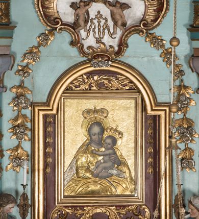 Zdjęcie nr 6: Nastawa ołtarzowa architektoniczna, jednoosiowa, jednokondygnacyjna ze zwieńczeniem, ustawiona na dwustrefowym cokole, z wyodrębnionymi dwiema parami prostopadłościanów. Ołtarz kamienny, wolnostojący, ustawiony na dwustopniowej podstawie, ujęty po bokach fryzowanymi konsolami. Mensa kamienna z marmurowym portatylem. Na przedniej ściance wyrzeźbiona w licu płycina, ujęta kanelowanymi lizenami, z monogramem IHS w polu. Na ołtarzu ustawione tabernakulum z tronem wystawienia. Tabernakulum w formie drewnianej skrzynki z obitymi blachą prostokątnymi drzwiczkami, ujętymi ramą. W ich polu medalion z przedstawieniem pelikana karmiącego młode na tle krzyża. Tron wystawienia w formie obrotowej, trójdzielnej niszy o wykroju stojącego prostokąta zamkniętego stylizowanym łukiem półokrągłym, zwieńczonej gzymsem. Nisza flankowana dekoracją w postaci liści ostrokrzewu i kampanuli, na gzymsie rocaille. Tabernakulum i tron ujęte parą niższych kolumn o kapitelach kompozytowych, na wysokich cokołach, dźwigających imposty, na których stoją wazony oraz spływami zakończonymi cokołami z fragmentami przerwanego przyczółka, na których klęczą adorujące anioły. Spływy dekorowane rocaille'em z podwieszonymi kampanulami. Kondygnacja ujęta dwiema parami pilastrów i stojących przed nimi kolumn o kapitelach kompozytowych, ustawionymi delikatnie pod kątem względem lica, wewnętrzna para wysunięta do przodu. Po wewnętrznej stronie ołtarza para pilastrów, których konsole podtrzymują belkowanie, a trzony dekorowane są zwisami roślinnymi, na ich tle figury św. Joachima i św. Anny. Podpory dźwigają pełne belkowanie, wyłamane na ich osi, przerwane nad polem środkowym oraz fragmenty przerwanego, falistego przyczółka z siedzącymi puttami, a także wolutowe cokoły z wazonami na zewnętrznych krawędziach belkowania. Fryz dekorowany rozetami. W polu środkowym nisza w formie stojącego prostokąta zamkniętego łukiem półkolistym nadwieszonym, ujęta profilowaną ramą z mniejszym obrazem Matki Boskiej z Dzieciątkiem oraz przedstawieniem św. Klemensa na zasuwie. Powyżej rokokowy kartusz z monogramem Marii, na którym dwa putta trzymają koronę, z podwieszonymi zwisami kwiatowymi, ujmującymi ramę pola głównego poniżej. Zwieńczenie w formie stojącego prostokąta z wolutowymi uszakami, zamkniętego gzymsem w formie łuku odcinkowego nadwieszonego. W polu rzeźbiarskie przedstawienie półpostaci Boga Ojca pośród obłoków, na tle glorii promienistej, ujętego przez siedzące na gzymsie, adorujące aniołki. Ołtarz flankują umocowane do ścian konsole z figurami św. Piotra i św. Pawła. Struktura w całości polichromowana w kolorze jasnoniebieskim, z niebieskimi i bladoróżowymi detalami, kolumny, profile i ornamentyka złocone, detale srebrzone.  
