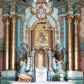 Zdjęcie nr 1: Nastawa ołtarzowa architektoniczna, jednoosiowa, jednokondygnacyjna ze zwieńczeniem, ustawiona na dwustrefowym cokole, z wyodrębnionymi dwiema parami prostopadłościanów. Ołtarz kamienny, wolnostojący, ustawiony na dwustopniowej podstawie, ujęty po bokach fryzowanymi konsolami. Mensa kamienna z marmurowym portatylem. Na przedniej ściance wyrzeźbiona w licu płycina, ujęta kanelowanymi lizenami, z monogramem IHS w polu. Na ołtarzu ustawione tabernakulum z tronem wystawienia. Tabernakulum w formie drewnianej skrzynki z obitymi blachą prostokątnymi drzwiczkami, ujętymi ramą. W ich polu medalion z przedstawieniem pelikana karmiącego młode na tle krzyża. Tron wystawienia w formie obrotowej, trójdzielnej niszy o wykroju stojącego prostokąta zamkniętego stylizowanym łukiem półokrągłym, zwieńczonej gzymsem. Nisza flankowana dekoracją w postaci liści ostrokrzewu i kampanuli, na gzymsie rocaille. Tabernakulum i tron ujęte parą niższych kolumn o kapitelach kompozytowych, na wysokich cokołach, dźwigających imposty, na których stoją wazony oraz spływami zakończonymi cokołami z fragmentami przerwanego przyczółka, na których klęczą adorujące anioły. Spływy dekorowane rocaille'em z podwieszonymi kampanulami. Kondygnacja ujęta dwiema parami pilastrów i stojących przed nimi kolumn o kapitelach kompozytowych, ustawionymi delikatnie pod kątem względem lica, wewnętrzna para wysunięta do przodu. Po wewnętrznej stronie ołtarza para pilastrów, których konsole podtrzymują belkowanie, a trzony dekorowane są zwisami roślinnymi, na ich tle figury św. Joachima i św. Anny. Podpory dźwigają pełne belkowanie, wyłamane na ich osi, przerwane nad polem środkowym oraz fragmenty przerwanego, falistego przyczółka z siedzącymi puttami, a także wolutowe cokoły z wazonami na zewnętrznych krawędziach belkowania. Fryz dekorowany rozetami. W polu środkowym nisza w formie stojącego prostokąta zamkniętego łukiem półkolistym nadwieszonym, ujęta profilowaną ramą z mniejszym obrazem Matki Boskiej z Dzieciątkiem oraz przedstawieniem św. Klemensa na zasuwie. Powyżej rokokowy kartusz z monogramem Marii, na którym dwa putta trzymają koronę, z podwieszonymi zwisami kwiatowymi, ujmującymi ramę pola głównego poniżej. Zwieńczenie w formie stojącego prostokąta z wolutowymi uszakami, zamkniętego gzymsem w formie łuku odcinkowego nadwieszonego. W polu rzeźbiarskie przedstawienie półpostaci Boga Ojca pośród obłoków, na tle glorii promienistej, ujętego przez siedzące na gzymsie, adorujące aniołki. Ołtarz flankują umocowane do ścian konsole z figurami św. Piotra i św. Pawła. Struktura w całości polichromowana w kolorze jasnoniebieskim, z niebieskimi i bladoróżowymi detalami, kolumny, profile i ornamentyka złocone, detale srebrzone.  
