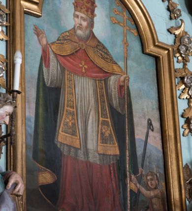 Zdjęcie nr 8: Nastawa ołtarzowa architektoniczna, jednoosiowa, jednokondygnacyjna ze zwieńczeniem, ustawiona na dwustrefowym cokole, z wyodrębnionymi dwiema parami prostopadłościanów. Ołtarz kamienny, wolnostojący, ustawiony na dwustopniowej podstawie, ujęty po bokach fryzowanymi konsolami. Mensa kamienna z marmurowym portatylem. Na przedniej ściance wyrzeźbiona w licu płycina, ujęta kanelowanymi lizenami, z monogramem IHS w polu. Na ołtarzu ustawione tabernakulum z tronem wystawienia. Tabernakulum w formie drewnianej skrzynki z obitymi blachą prostokątnymi drzwiczkami, ujętymi ramą. W ich polu medalion z przedstawieniem pelikana karmiącego młode na tle krzyża. Tron wystawienia w formie obrotowej, trójdzielnej niszy o wykroju stojącego prostokąta zamkniętego stylizowanym łukiem półokrągłym, zwieńczonej gzymsem. Nisza flankowana dekoracją w postaci liści ostrokrzewu i kampanuli, na gzymsie rocaille. Tabernakulum i tron ujęte parą niższych kolumn o kapitelach kompozytowych, na wysokich cokołach, dźwigających imposty, na których stoją wazony oraz spływami zakończonymi cokołami z fragmentami przerwanego przyczółka, na których klęczą adorujące anioły. Spływy dekorowane rocaille'em z podwieszonymi kampanulami. Kondygnacja ujęta dwiema parami pilastrów i stojących przed nimi kolumn o kapitelach kompozytowych, ustawionymi delikatnie pod kątem względem lica, wewnętrzna para wysunięta do przodu. Po wewnętrznej stronie ołtarza para pilastrów, których konsole podtrzymują belkowanie, a trzony dekorowane są zwisami roślinnymi, na ich tle figury św. Joachima i św. Anny. Podpory dźwigają pełne belkowanie, wyłamane na ich osi, przerwane nad polem środkowym oraz fragmenty przerwanego, falistego przyczółka z siedzącymi puttami, a także wolutowe cokoły z wazonami na zewnętrznych krawędziach belkowania. Fryz dekorowany rozetami. W polu środkowym nisza w formie stojącego prostokąta zamkniętego łukiem półkolistym nadwieszonym, ujęta profilowaną ramą z mniejszym obrazem Matki Boskiej z Dzieciątkiem oraz przedstawieniem św. Klemensa na zasuwie. Powyżej rokokowy kartusz z monogramem Marii, na którym dwa putta trzymają koronę, z podwieszonymi zwisami kwiatowymi, ujmującymi ramę pola głównego poniżej. Zwieńczenie w formie stojącego prostokąta z wolutowymi uszakami, zamkniętego gzymsem w formie łuku odcinkowego nadwieszonego. W polu rzeźbiarskie przedstawienie półpostaci Boga Ojca pośród obłoków, na tle glorii promienistej, ujętego przez siedzące na gzymsie, adorujące aniołki. Ołtarz flankują umocowane do ścian konsole z figurami św. Piotra i św. Pawła. Struktura w całości polichromowana w kolorze jasnoniebieskim, z niebieskimi i bladoróżowymi detalami, kolumny, profile i ornamentyka złocone, detale srebrzone.  
