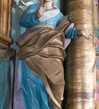 Zdjęcie nr 37: Nastawa ołtarzowa architektoniczna, jednoosiowa, jednokondygnacyjna ze zwieńczeniem, ustawiona na dwustrefowym cokole, z wyodrębnionymi dwiema parami prostopadłościanów. Ołtarz kamienny, wolnostojący, ustawiony na dwustopniowej podstawie, ujęty po bokach fryzowanymi konsolami. Mensa kamienna z marmurowym portatylem. Na przedniej ściance wyrzeźbiona w licu płycina, ujęta kanelowanymi lizenami, z monogramem IHS w polu. Na ołtarzu ustawione tabernakulum z tronem wystawienia. Tabernakulum w formie drewnianej skrzynki z obitymi blachą prostokątnymi drzwiczkami, ujętymi ramą. W ich polu medalion z przedstawieniem pelikana karmiącego młode na tle krzyża. Tron wystawienia w formie obrotowej, trójdzielnej niszy o wykroju stojącego prostokąta zamkniętego stylizowanym łukiem półokrągłym, zwieńczonej gzymsem. Nisza flankowana dekoracją w postaci liści ostrokrzewu i kampanuli, na gzymsie rocaille. Tabernakulum i tron ujęte parą niższych kolumn o kapitelach kompozytowych, na wysokich cokołach, dźwigających imposty, na których stoją wazony oraz spływami zakończonymi cokołami z fragmentami przerwanego przyczółka, na których klęczą adorujące anioły. Spływy dekorowane rocaille'em z podwieszonymi kampanulami. Kondygnacja ujęta dwiema parami pilastrów i stojących przed nimi kolumn o kapitelach kompozytowych, ustawionymi delikatnie pod kątem względem lica, wewnętrzna para wysunięta do przodu. Po wewnętrznej stronie ołtarza para pilastrów, których konsole podtrzymują belkowanie, a trzony dekorowane są zwisami roślinnymi, na ich tle figury św. Joachima i św. Anny. Podpory dźwigają pełne belkowanie, wyłamane na ich osi, przerwane nad polem środkowym oraz fragmenty przerwanego, falistego przyczółka z siedzącymi puttami, a także wolutowe cokoły z wazonami na zewnętrznych krawędziach belkowania. Fryz dekorowany rozetami. W polu środkowym nisza w formie stojącego prostokąta zamkniętego łukiem półkolistym nadwieszonym, ujęta profilowaną ramą z mniejszym obrazem Matki Boskiej z Dzieciątkiem oraz przedstawieniem św. Klemensa na zasuwie. Powyżej rokokowy kartusz z monogramem Marii, na którym dwa putta trzymają koronę, z podwieszonymi zwisami kwiatowymi, ujmującymi ramę pola głównego poniżej. Zwieńczenie w formie stojącego prostokąta z wolutowymi uszakami, zamkniętego gzymsem w formie łuku odcinkowego nadwieszonego. W polu rzeźbiarskie przedstawienie półpostaci Boga Ojca pośród obłoków, na tle glorii promienistej, ujętego przez siedzące na gzymsie, adorujące aniołki. Ołtarz flankują umocowane do ścian konsole z figurami św. Piotra i św. Pawła. Struktura w całości polichromowana w kolorze jasnoniebieskim, z niebieskimi i bladoróżowymi detalami, kolumny, profile i ornamentyka złocone, detale srebrzone.  
