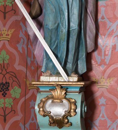 Zdjęcie nr 22: Nastawa ołtarzowa architektoniczna, jednoosiowa, jednokondygnacyjna ze zwieńczeniem, ustawiona na dwustrefowym cokole, z wyodrębnionymi dwiema parami prostopadłościanów. Ołtarz kamienny, wolnostojący, ustawiony na dwustopniowej podstawie, ujęty po bokach fryzowanymi konsolami. Mensa kamienna z marmurowym portatylem. Na przedniej ściance wyrzeźbiona w licu płycina, ujęta kanelowanymi lizenami, z monogramem IHS w polu. Na ołtarzu ustawione tabernakulum z tronem wystawienia. Tabernakulum w formie drewnianej skrzynki z obitymi blachą prostokątnymi drzwiczkami, ujętymi ramą. W ich polu medalion z przedstawieniem pelikana karmiącego młode na tle krzyża. Tron wystawienia w formie obrotowej, trójdzielnej niszy o wykroju stojącego prostokąta zamkniętego stylizowanym łukiem półokrągłym, zwieńczonej gzymsem. Nisza flankowana dekoracją w postaci liści ostrokrzewu i kampanuli, na gzymsie rocaille. Tabernakulum i tron ujęte parą niższych kolumn o kapitelach kompozytowych, na wysokich cokołach, dźwigających imposty, na których stoją wazony oraz spływami zakończonymi cokołami z fragmentami przerwanego przyczółka, na których klęczą adorujące anioły. Spływy dekorowane rocaille'em z podwieszonymi kampanulami. Kondygnacja ujęta dwiema parami pilastrów i stojących przed nimi kolumn o kapitelach kompozytowych, ustawionymi delikatnie pod kątem względem lica, wewnętrzna para wysunięta do przodu. Po wewnętrznej stronie ołtarza para pilastrów, których konsole podtrzymują belkowanie, a trzony dekorowane są zwisami roślinnymi, na ich tle figury św. Joachima i św. Anny. Podpory dźwigają pełne belkowanie, wyłamane na ich osi, przerwane nad polem środkowym oraz fragmenty przerwanego, falistego przyczółka z siedzącymi puttami, a także wolutowe cokoły z wazonami na zewnętrznych krawędziach belkowania. Fryz dekorowany rozetami. W polu środkowym nisza w formie stojącego prostokąta zamkniętego łukiem półkolistym nadwieszonym, ujęta profilowaną ramą z mniejszym obrazem Matki Boskiej z Dzieciątkiem oraz przedstawieniem św. Klemensa na zasuwie. Powyżej rokokowy kartusz z monogramem Marii, na którym dwa putta trzymają koronę, z podwieszonymi zwisami kwiatowymi, ujmującymi ramę pola głównego poniżej. Zwieńczenie w formie stojącego prostokąta z wolutowymi uszakami, zamkniętego gzymsem w formie łuku odcinkowego nadwieszonego. W polu rzeźbiarskie przedstawienie półpostaci Boga Ojca pośród obłoków, na tle glorii promienistej, ujętego przez siedzące na gzymsie, adorujące aniołki. Ołtarz flankują umocowane do ścian konsole z figurami św. Piotra i św. Pawła. Struktura w całości polichromowana w kolorze jasnoniebieskim, z niebieskimi i bladoróżowymi detalami, kolumny, profile i ornamentyka złocone, detale srebrzone.  
