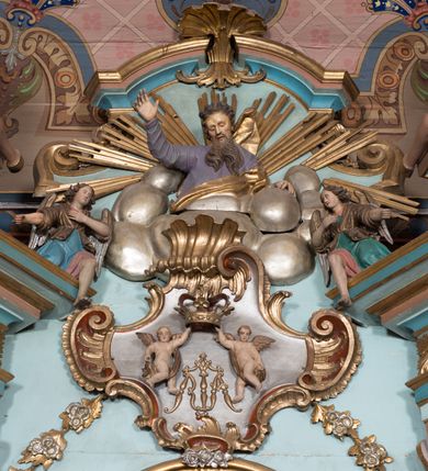 Zdjęcie nr 12: Nastawa ołtarzowa architektoniczna, jednoosiowa, jednokondygnacyjna ze zwieńczeniem, ustawiona na dwustrefowym cokole, z wyodrębnionymi dwiema parami prostopadłościanów. Ołtarz kamienny, wolnostojący, ustawiony na dwustopniowej podstawie, ujęty po bokach fryzowanymi konsolami. Mensa kamienna z marmurowym portatylem. Na przedniej ściance wyrzeźbiona w licu płycina, ujęta kanelowanymi lizenami, z monogramem IHS w polu. Na ołtarzu ustawione tabernakulum z tronem wystawienia. Tabernakulum w formie drewnianej skrzynki z obitymi blachą prostokątnymi drzwiczkami, ujętymi ramą. W ich polu medalion z przedstawieniem pelikana karmiącego młode na tle krzyża. Tron wystawienia w formie obrotowej, trójdzielnej niszy o wykroju stojącego prostokąta zamkniętego stylizowanym łukiem półokrągłym, zwieńczonej gzymsem. Nisza flankowana dekoracją w postaci liści ostrokrzewu i kampanuli, na gzymsie rocaille. Tabernakulum i tron ujęte parą niższych kolumn o kapitelach kompozytowych, na wysokich cokołach, dźwigających imposty, na których stoją wazony oraz spływami zakończonymi cokołami z fragmentami przerwanego przyczółka, na których klęczą adorujące anioły. Spływy dekorowane rocaille'em z podwieszonymi kampanulami. Kondygnacja ujęta dwiema parami pilastrów i stojących przed nimi kolumn o kapitelach kompozytowych, ustawionymi delikatnie pod kątem względem lica, wewnętrzna para wysunięta do przodu. Po wewnętrznej stronie ołtarza para pilastrów, których konsole podtrzymują belkowanie, a trzony dekorowane są zwisami roślinnymi, na ich tle figury św. Joachima i św. Anny. Podpory dźwigają pełne belkowanie, wyłamane na ich osi, przerwane nad polem środkowym oraz fragmenty przerwanego, falistego przyczółka z siedzącymi puttami, a także wolutowe cokoły z wazonami na zewnętrznych krawędziach belkowania. Fryz dekorowany rozetami. W polu środkowym nisza w formie stojącego prostokąta zamkniętego łukiem półkolistym nadwieszonym, ujęta profilowaną ramą z mniejszym obrazem Matki Boskiej z Dzieciątkiem oraz przedstawieniem św. Klemensa na zasuwie. Powyżej rokokowy kartusz z monogramem Marii, na którym dwa putta trzymają koronę, z podwieszonymi zwisami kwiatowymi, ujmującymi ramę pola głównego poniżej. Zwieńczenie w formie stojącego prostokąta z wolutowymi uszakami, zamkniętego gzymsem w formie łuku odcinkowego nadwieszonego. W polu rzeźbiarskie przedstawienie półpostaci Boga Ojca pośród obłoków, na tle glorii promienistej, ujętego przez siedzące na gzymsie, adorujące aniołki. Ołtarz flankują umocowane do ścian konsole z figurami św. Piotra i św. Pawła. Struktura w całości polichromowana w kolorze jasnoniebieskim, z niebieskimi i bladoróżowymi detalami, kolumny, profile i ornamentyka złocone, detale srebrzone.  
