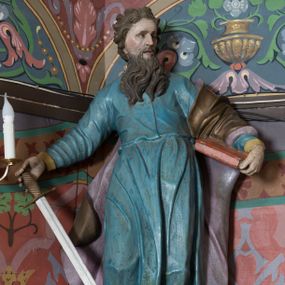 Zdjęcie nr 1: Na konsoli umocowanej do ściany zamykającej prezbiterium, po prawej stronie ołtarza ustawiona figura św. Pawła. Konsola dekorowana rokokowym kartuszem z zasrebrzonym podpisem „ŚW(IĘTY) PAWEŁ”. Rzeźba drążona, zwrócona w trzech czwartych w lewo, w kontrapoście, odchylona w tył. Święty lewą ręką podtrzymuje opartą na boku księgę, w prawej trzyma zwrócony ostrzem w dół miecz. Twarz ma szczupłą, pociągłą, o starczych rysach, blisko siebie osadzonych oczach, garbatym nosie i otwartych, wąskich ustach, okoloną brązową, długą brodą oraz brązowymi, krótkimi i kręconymi włosami. Święty ubrany jest w długą tunikę, o wąskich rękawach, przepasaną w talii oraz złocony płaszcz z jasnofioletową podszewką, przerzucony przez lewe ramie i opadający na plecy, z rozwianą na boki, drapowaną tkaniną. Polichromia ciała naturalistyczna. 