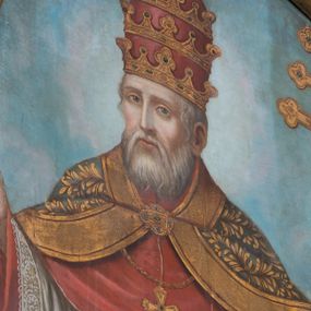 Zdjęcie nr 1: Obraz w formie stojącego prostokąta zamkniętego łukiem półkolistym nadwieszonym. W centrum całopostaciowe przedstawienie św. Klemensa zwróconego frontalnie, z głową skierowaną w prawo. Święty ma ręce rozłożone na boki, w lewej trzyma ferulę, prawą dłoń unosi w geście błogosławieństwa. Twarz ma pociągłą, o łagodnych rysach, dużych, głęboko osadzonych oczach, prostym, wąskim nosie, okoloną białą brodą i krótkimi, siwymi włosami. Ubrany jest w czerwoną sutannę o szerokich rękawach, rokietę dekorowaną koronką przy brzegach, obie obficie drapowane w drobne rurkowate fałdki. Na nich stuła o złoconym wzorze, czerwony mucet i pektorał. Święty ma narzuconą na ramiona zieloną kapę o wzorze roślinnym z grubą, złoconą lamówką, zapiętą dekoracyjną klamrą pod szyją. Na głowie ma tiarę. W prawym dolnym rogu obrazu siedzące putto, zwrócone w trzech czwartych w prawo, podtrzymujące kotwicę. Święty ukazany jest na tle górzystego pejzażu z horyzontem na jednej trzeciej wysokości obrazu, powyżej błękitno-różowe, rozświetlone niebo. 
