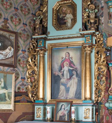 Zdjęcie nr 1: Nastawa ołtarzowa architektoniczna, jednoosiowa, jednokondygnacyjna ze zwieńczeniem ustawiona na cokole z wyodrębnionymi po bokach prostopadłościanami. Ołtarz kamienny prostopadłościenny, ujęty po bokach esownicami, z przodu flankowany kanelowanymi lizenami, w centrum płaskorzeźbione gorejące serce. Nastawa flankowana parą kolumn o kapitelach korynckich, dźwigających belkowanie wyłamane na ich osi, przerwane przez pole środkowe, w partii fryzu dekorowane rozetami. Całe pole środkowe wypełnia nisza w formie stojącego prostokąta z obrazem Matki Boskiej Różańcowej ze św. Dominikiem i św. Katarzyną Sieneńską, ujęta złoconą, profilowaną ramą. Na belkowaniu ustawione dwa wazony z bukietami kwiatów. Kondygnacja flankowana uszami utworzonymi z ażurowego akantu z kampanulami. Zwieńczenie w formie stojącego prostokąta zakończonego kluczem z rozetą, ujętego z trzech stron ażurowym akantem. W polu obraz św. Józefa z Dzieciątkiem w formie stojącego prostokąta o ściętych narożach, w ramie dekorowanej ażurowym ornamentem roślinnym. Całość zakończona medalionem z monogramem Marii otoczonym obłokami, w glorii promienistej. Struktura polichromowana w kolorze jasnoniebieskim, z niebieskimi i czerwonymi detalami, kolumny, profile i ornamentyka złocone, elementy dekoracji srebrzone. 