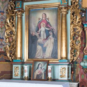 Zdjęcie nr 1: Nastawa ołtarzowa architektoniczna, jednoosiowa, jednokondygnacyjna ze zwieńczeniem ustawiona na cokole z wyodrębnionymi po bokach prostopadłościanami. Ołtarz kamienny prostopadłościenny, ujęty po bokach esownicami, z przodu flankowany kanelowanymi lizenami, w centrum płaskorzeźbione gorejące serce. Nastawa flankowana parą kolumn o kapitelach korynckich, dźwigających belkowanie wyłamane na ich osi, przerwane przez pole środkowe, w partii fryzu dekorowane rozetami. Całe pole środkowe wypełnia nisza w formie stojącego prostokąta z obrazem Matki Boskiej Różańcowej ze św. Dominikiem i św. Katarzyną Sieneńską, ujęta złoconą, profilowaną ramą. Na belkowaniu ustawione dwa wazony z bukietami kwiatów. Kondygnacja flankowana uszami utworzonymi z ażurowego akantu z kampanulami. Zwieńczenie w formie stojącego prostokąta zakończonego kluczem z rozetą, ujętego z trzech stron ażurowym akantem. W polu obraz św. Józefa z Dzieciątkiem w formie stojącego prostokąta o ściętych narożach, w ramie dekorowanej ażurowym ornamentem roślinnym. Całość zakończona medalionem z monogramem Marii otoczonym obłokami, w glorii promienistej. Struktura polichromowana w kolorze jasnoniebieskim, z niebieskimi i czerwonymi detalami, kolumny, profile i ornamentyka złocone, elementy dekoracji srebrzone. 