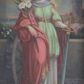 Zdjęcie nr 1: Obraz w formie stojącego prostokąta z przedstawieniem św. Katarzyny Aleksandryjskiej. Święta ukazana w całej postaci, frontalnie, w kontrapoście. W lewej ręce trzyma rękojeść miecza zwróconego ostrzem w dół, prawy łokieć opiera na stojącym obok kole, w dłoni trzyma liść palmy i gałązkę lilii. Katarzyna ma owalną twarz z okrągłymi oczami, prostym nosem i pełnymi ustami, okoloną długimi, brązowymi włosami opadającymi na ramiona. Ubrana jest w białą, długą suknię spodnią ze złoconą lamówką, jasnozieloną suknię wierzchnią sięgającą kolan, ze złotym pasem w talii, na ramiona ma narzucony czerwony płaszcz ze złotą lamówką, opadający na prawą nogę i bok postaci. Pod szyją ma białą podwikę, na głowie zaś półprzeźroczysty welon i diadem. Święta ukazana na tle niskiego muru i kamiennej posadzki, z widocznym w tle pejzażem z wieżą po lewej stronie. Zachmurzone niebo rozstępuje się wokół głowy świętej, na którą padają promienie światła. W prawym dolnym rogu sygnatura „pinx[it] / M[arian] Szczurowski / 1910”. 