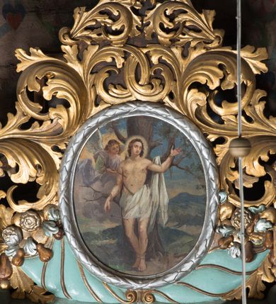Zdjęcie nr 3: Obraz w formie stojącego owalu z przedstawieniem św. Sebastiana przywiązanego do drzewa. Święty ukazany jest w całej postaci, frontalnie, w kontrapoście. Lewą rękę ma uniesioną, prawą opadającą wzdłuż boku, obie przywiązane do gałęzi drzewa. Twarz ma okrągłą, o zamkniętych oczach i prostym nosie, okoloną krótkimi, brązowymi włosami. Wokół głowy nimb. Jego ciało jest umięśnione o rozbudowanej klatce piersiowej, w partii bioder przesłonięte białą tkaniną, której część zawieszona jest na drzewie po lewej stronie świętego. Po jego prawej widoczny nadlatujący na obłoku anioł, który wyciąga z jego boku strzałę. Scena ukazana jest na tle górzystego pejzażu. 